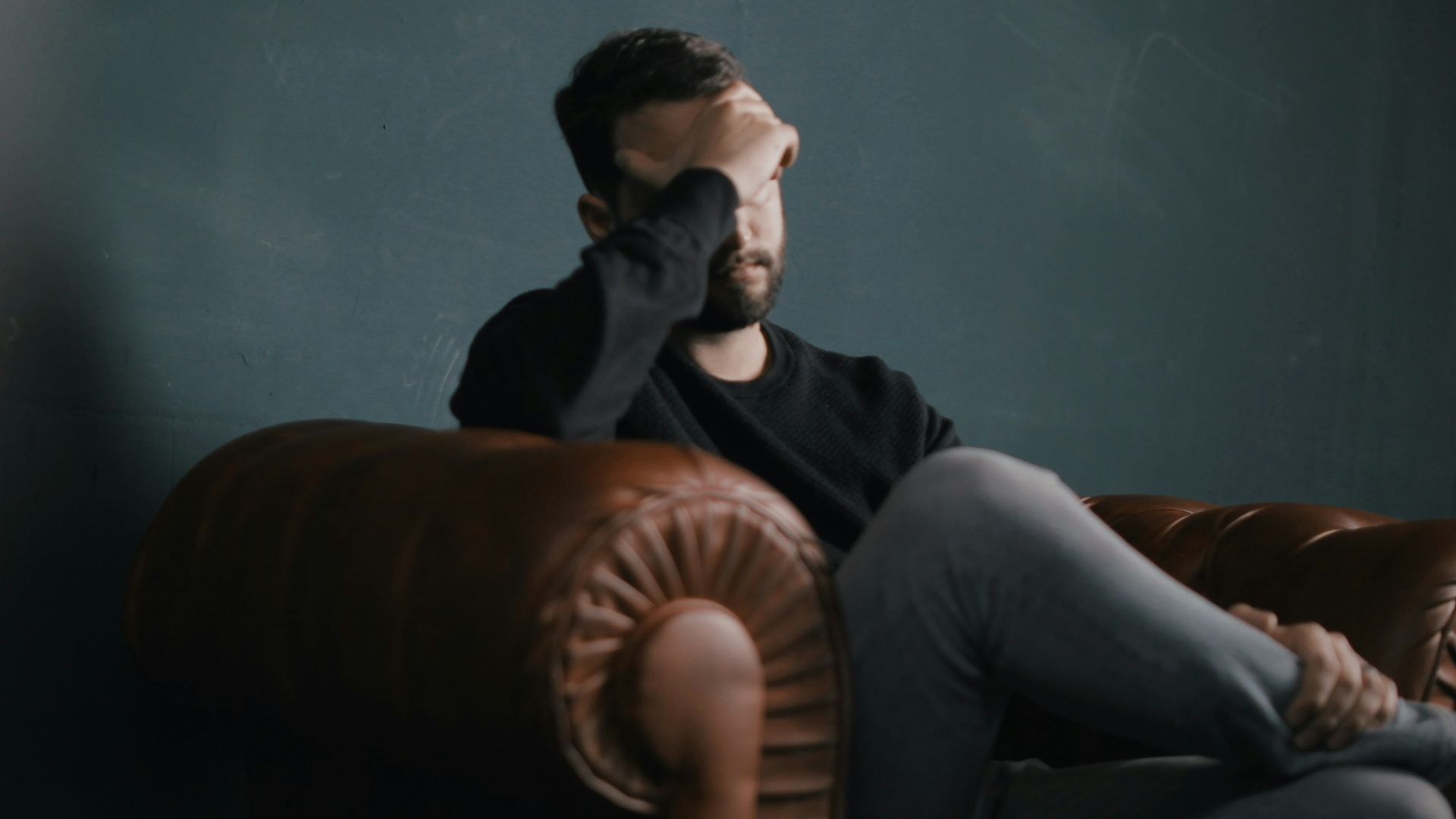 a man holds his head while sitting on a sofa