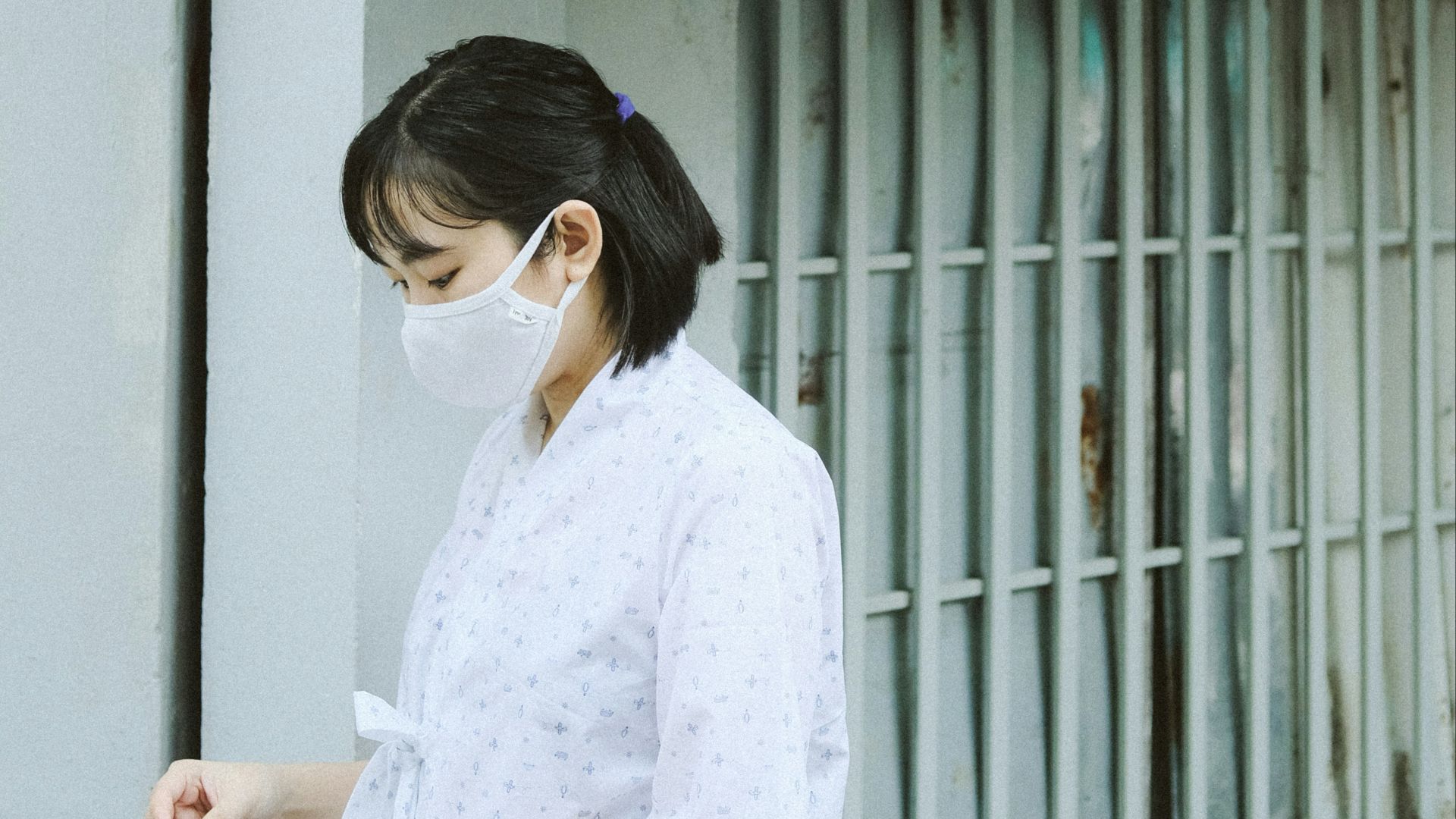 a woman wearing a face mask standing in front of a fence