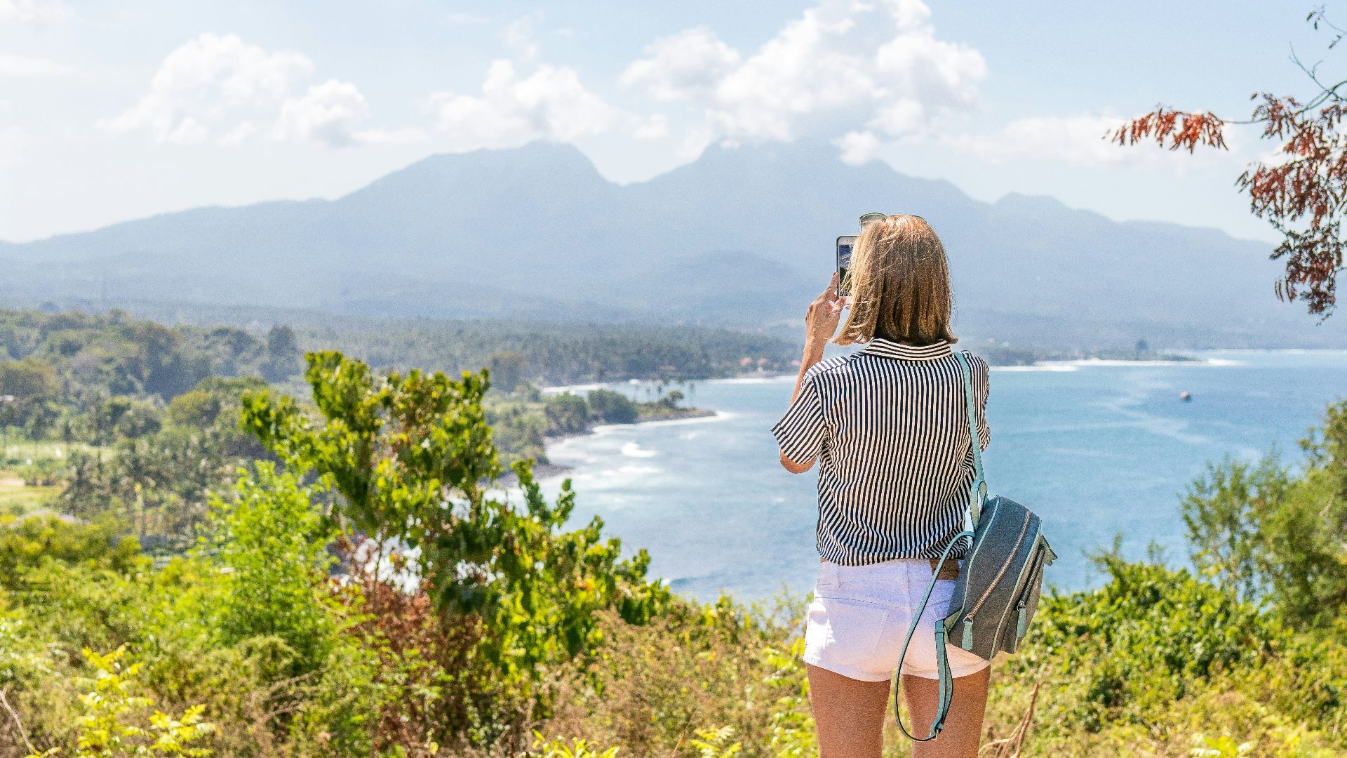 a woman taking a picture of the ocean with her cell phone