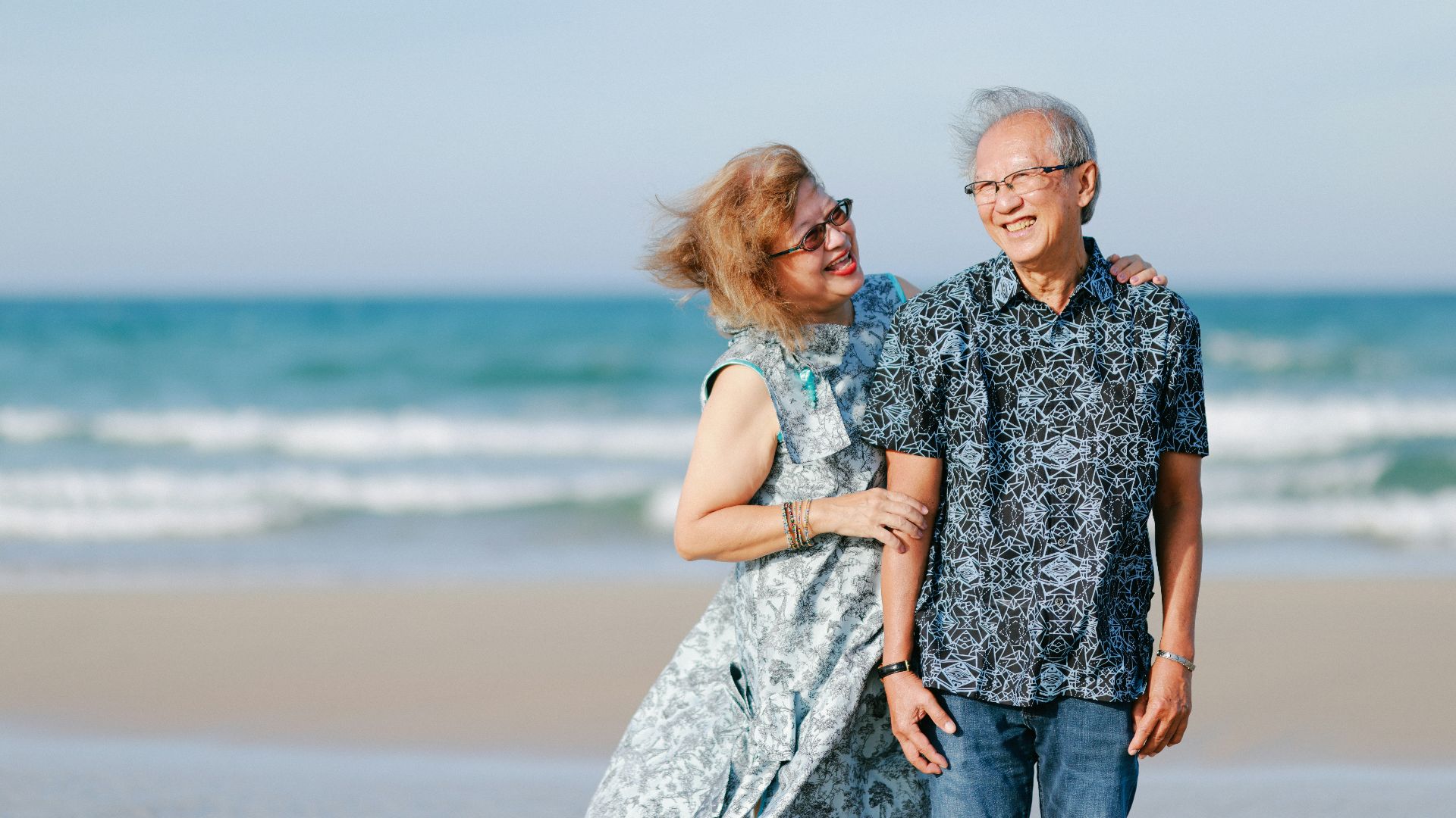 Elderly couple smiling on a sandy beach.