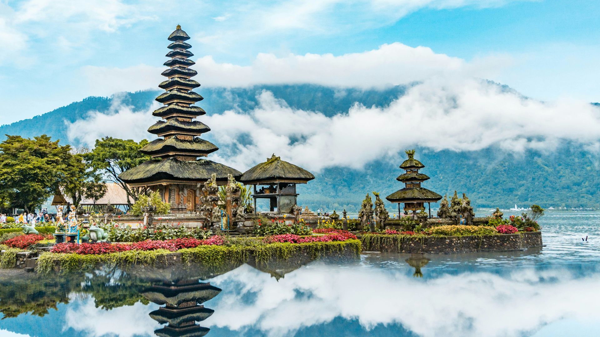 brown and green temple near body of water under blue and white cloudy sky during daytime