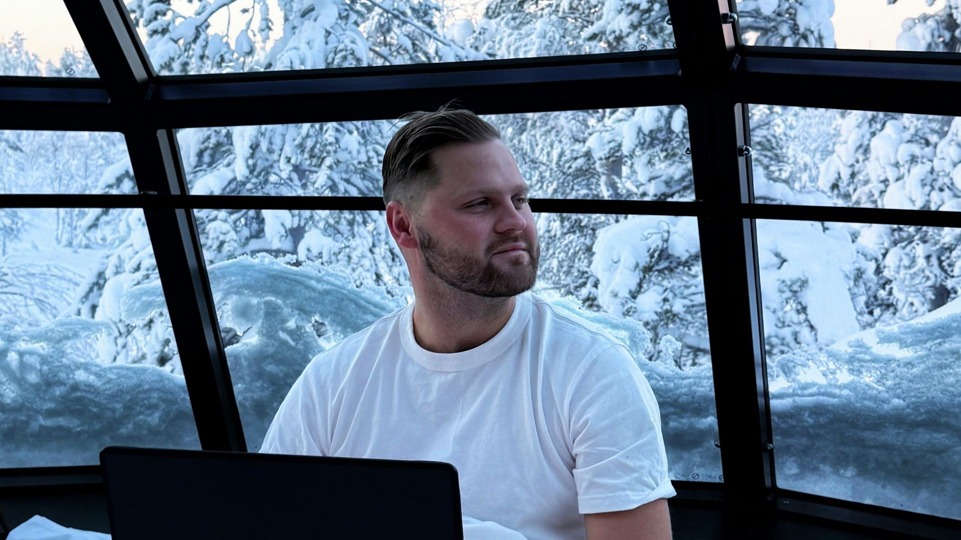 Man working on a laptop with a snowy forest view.
