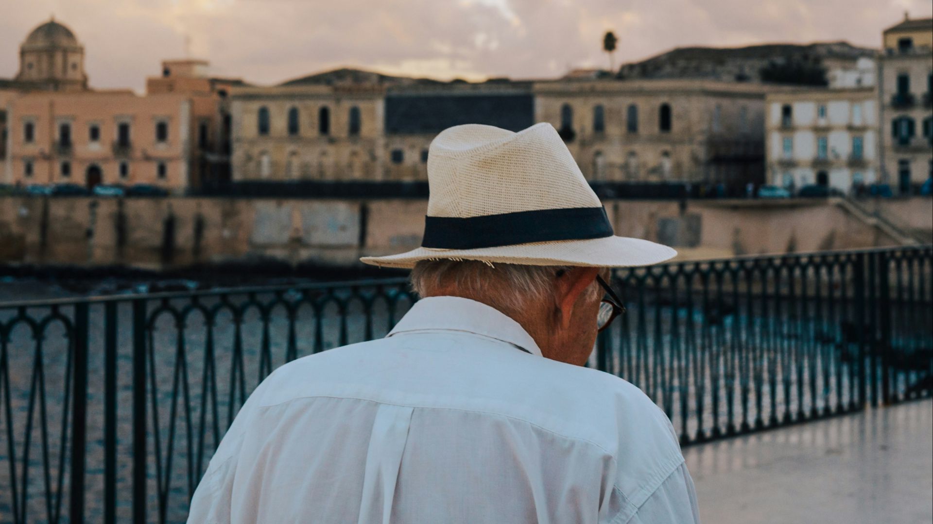 Man in hat walks by old buildings at sunset