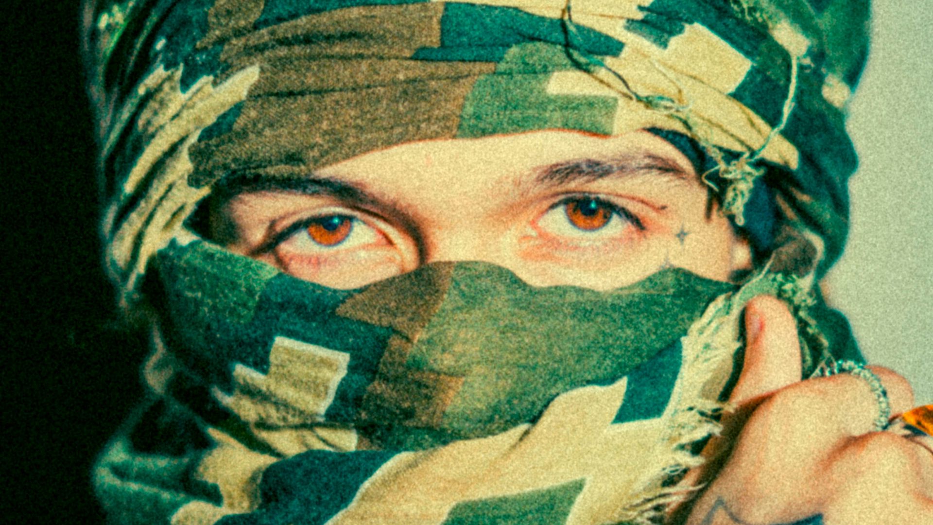 Man with camouflage face covering and spiderweb tattoo