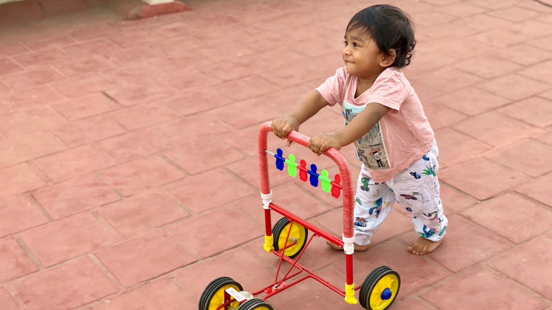 girl in white and pink floral dress riding red and yellow trike
