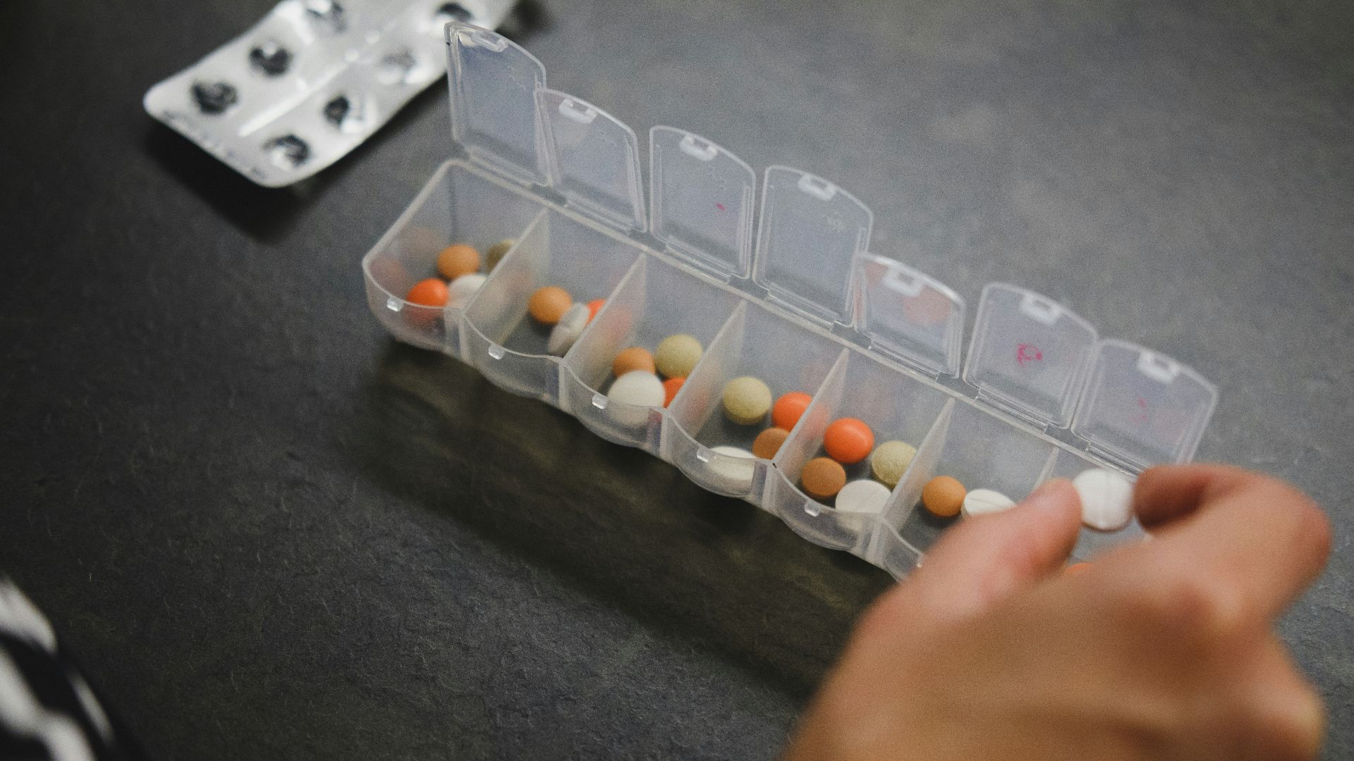 person about to pick medicine from medicine organizer