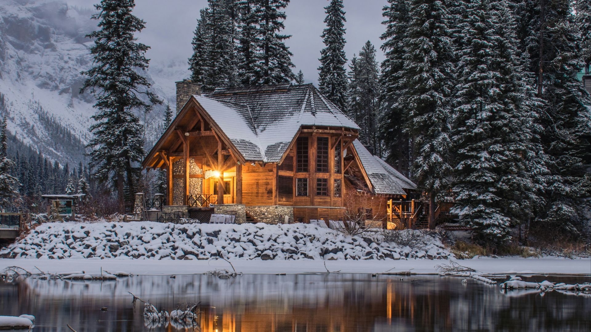 wooden house near pine trees and pond coated with snow during daytime