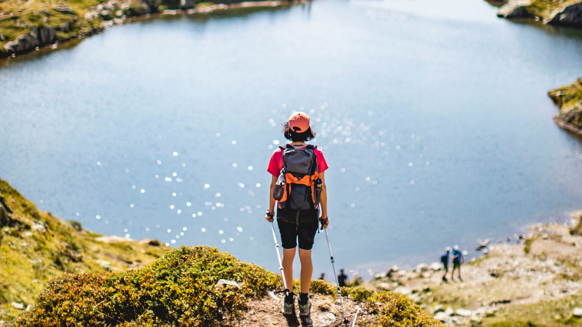 man in red jacket and black pants standing on rock near lake during daytime