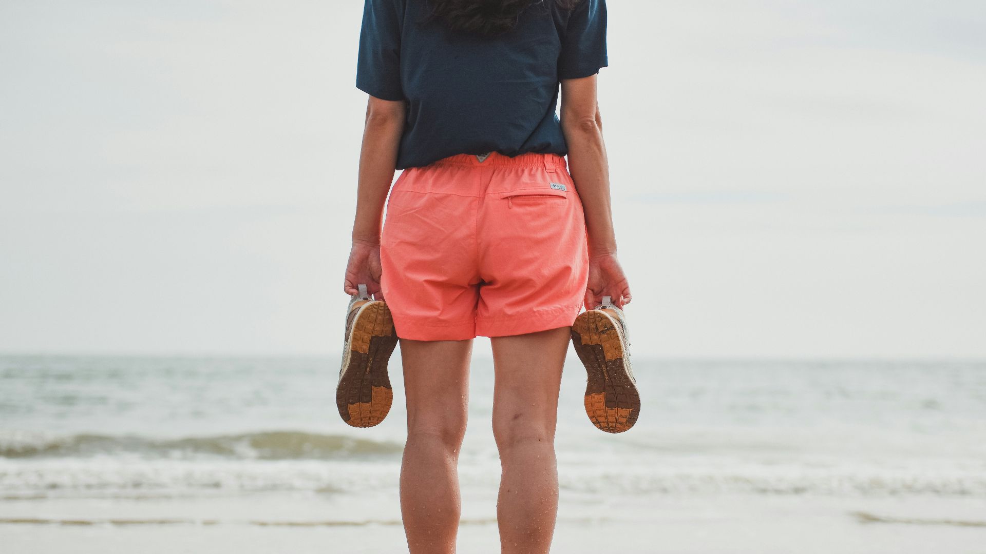 man in blue shirt and orange shorts standing on beach during daytime