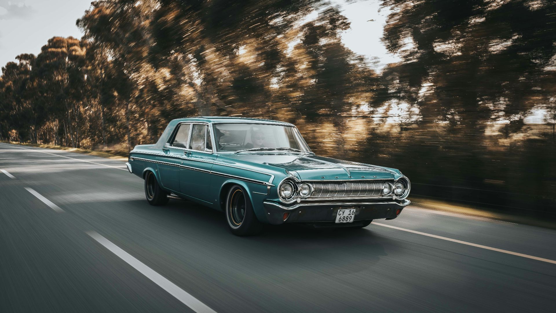 teal sedan on roadway beside the trees