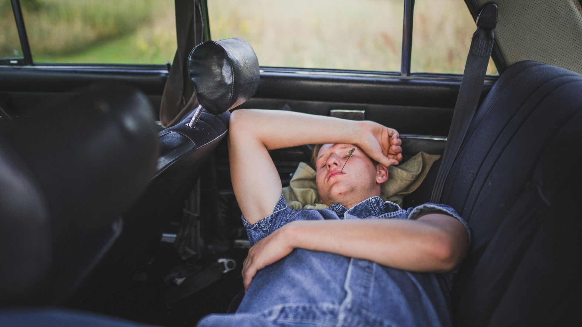 person in blue denim shirt sleeping behind the car seat