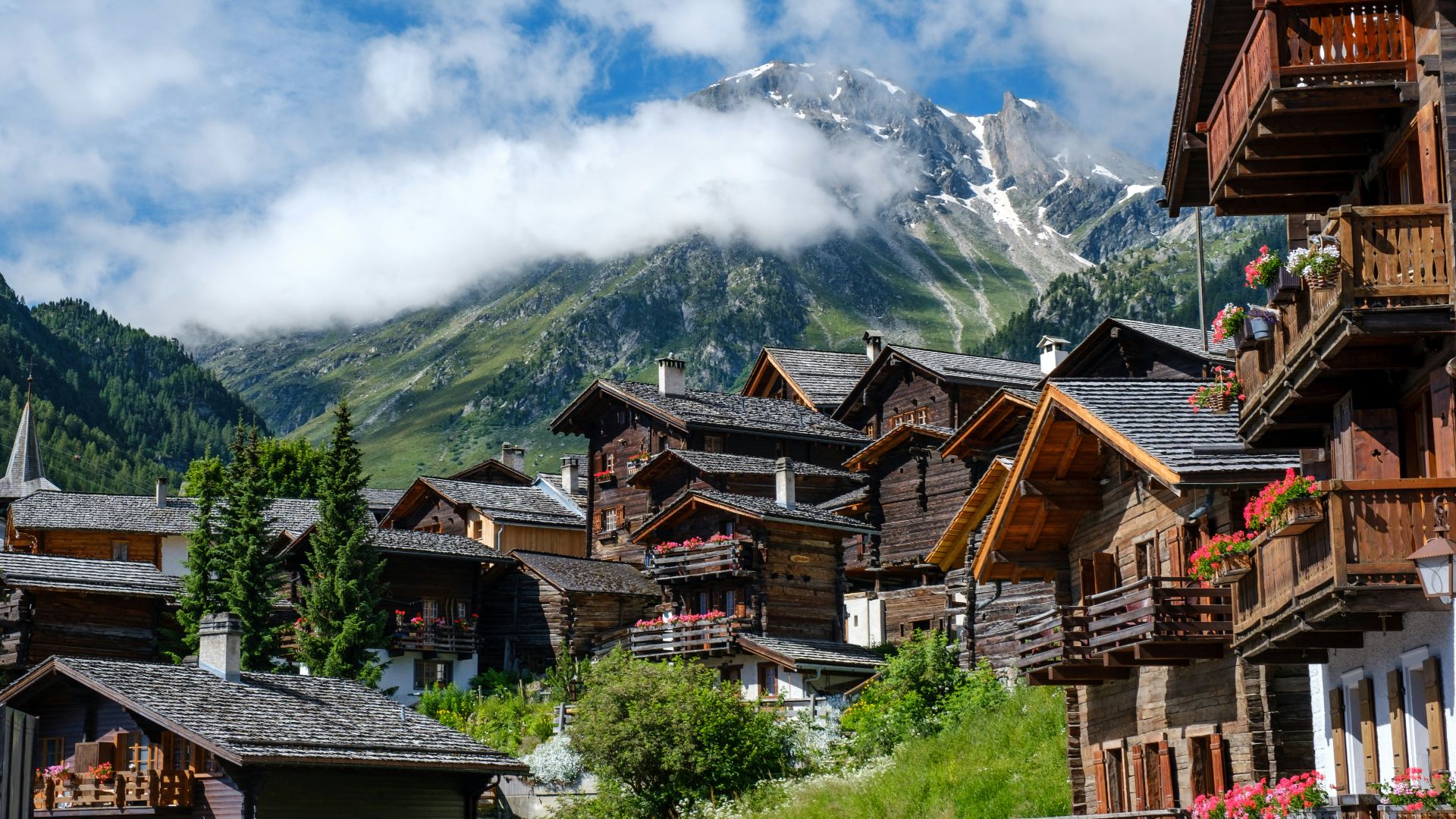brown wooden houses near green trees and mountain under white clouds during daytime