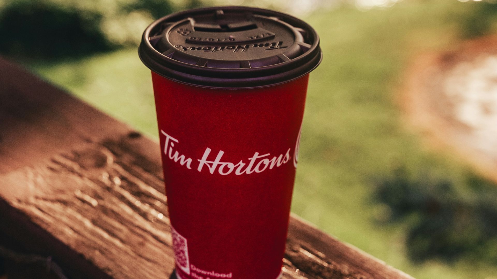 A red coffee cup sitting on top of a wooden railing