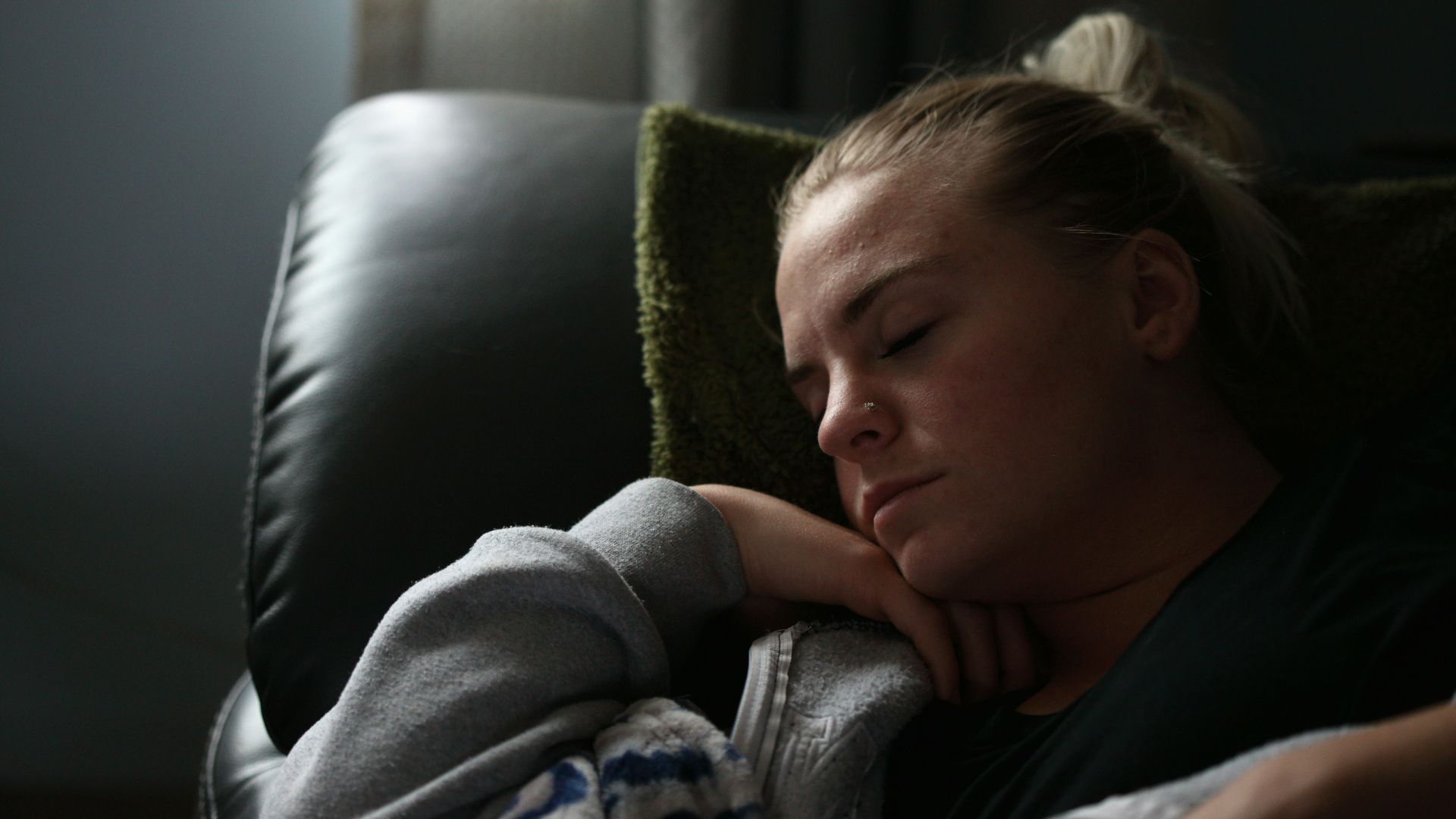 boy in gray hoodie lying on black leather couch