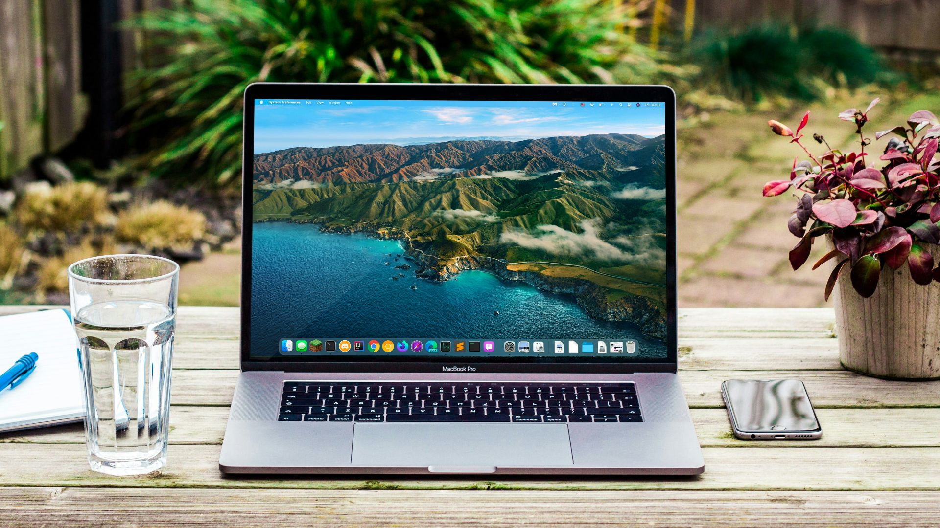 macbook pro beside clear drinking glass on brown wooden table