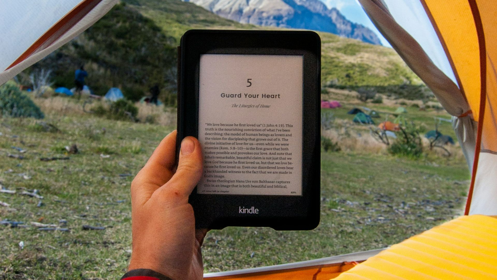 person holding black Amazon Kindle E-Book reader inside tent at daytime