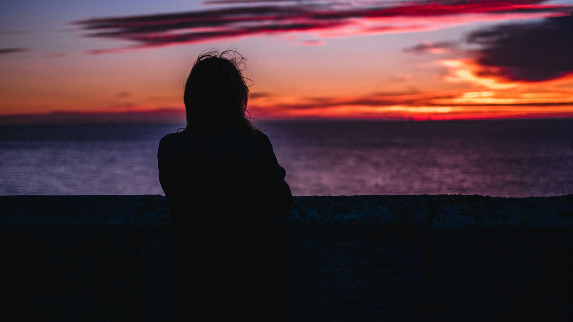 silhouette photo of person standing while looking at the ocean during golden hour