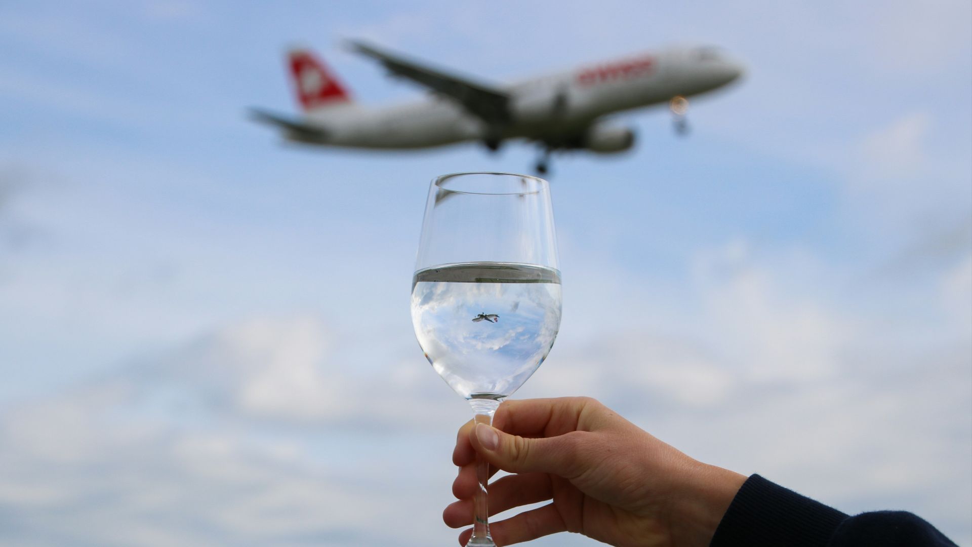 person holding clear wine glass with white airplane in the sky