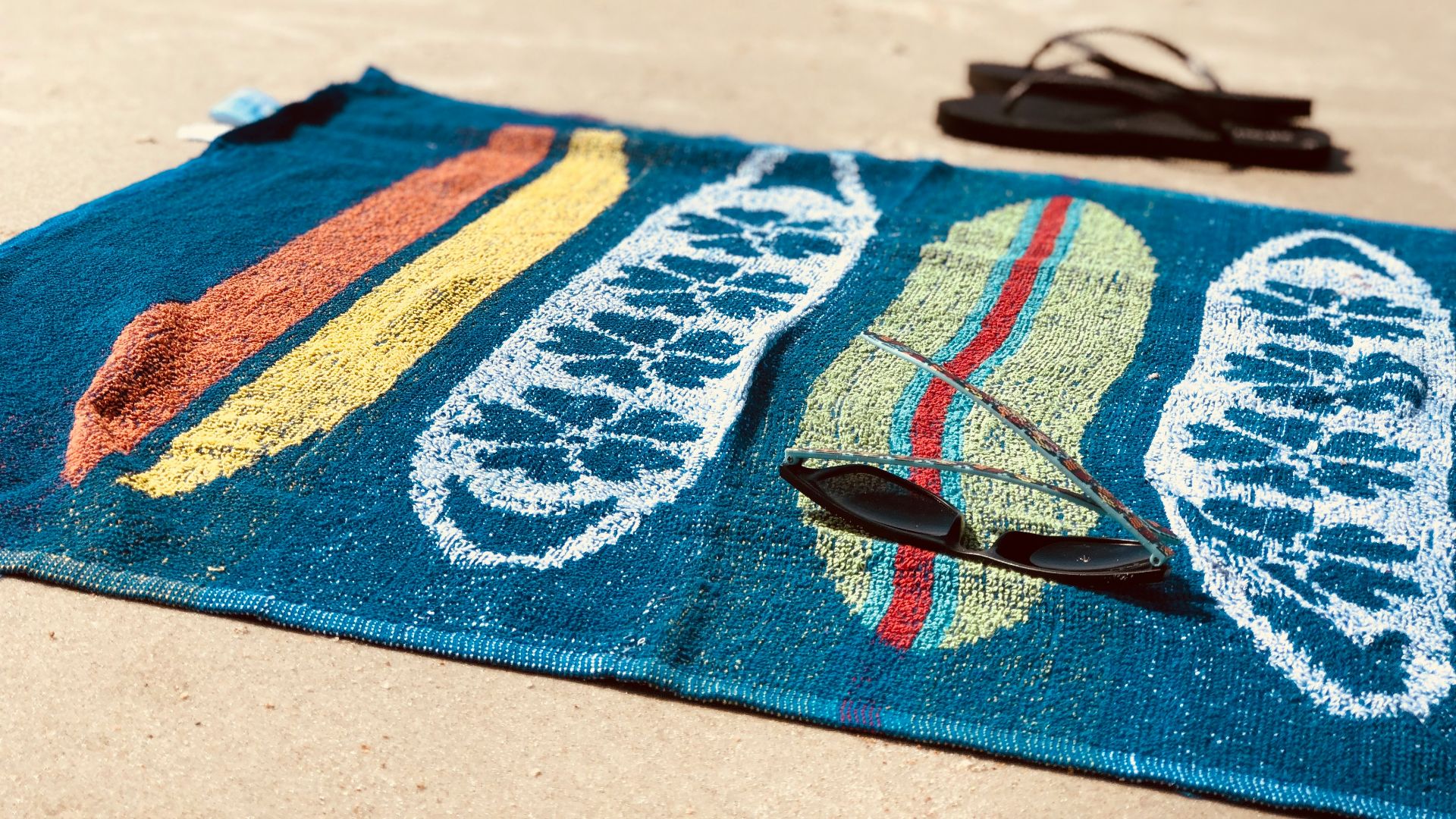 black sunglasses on blue towel beside pair of black flip-flops