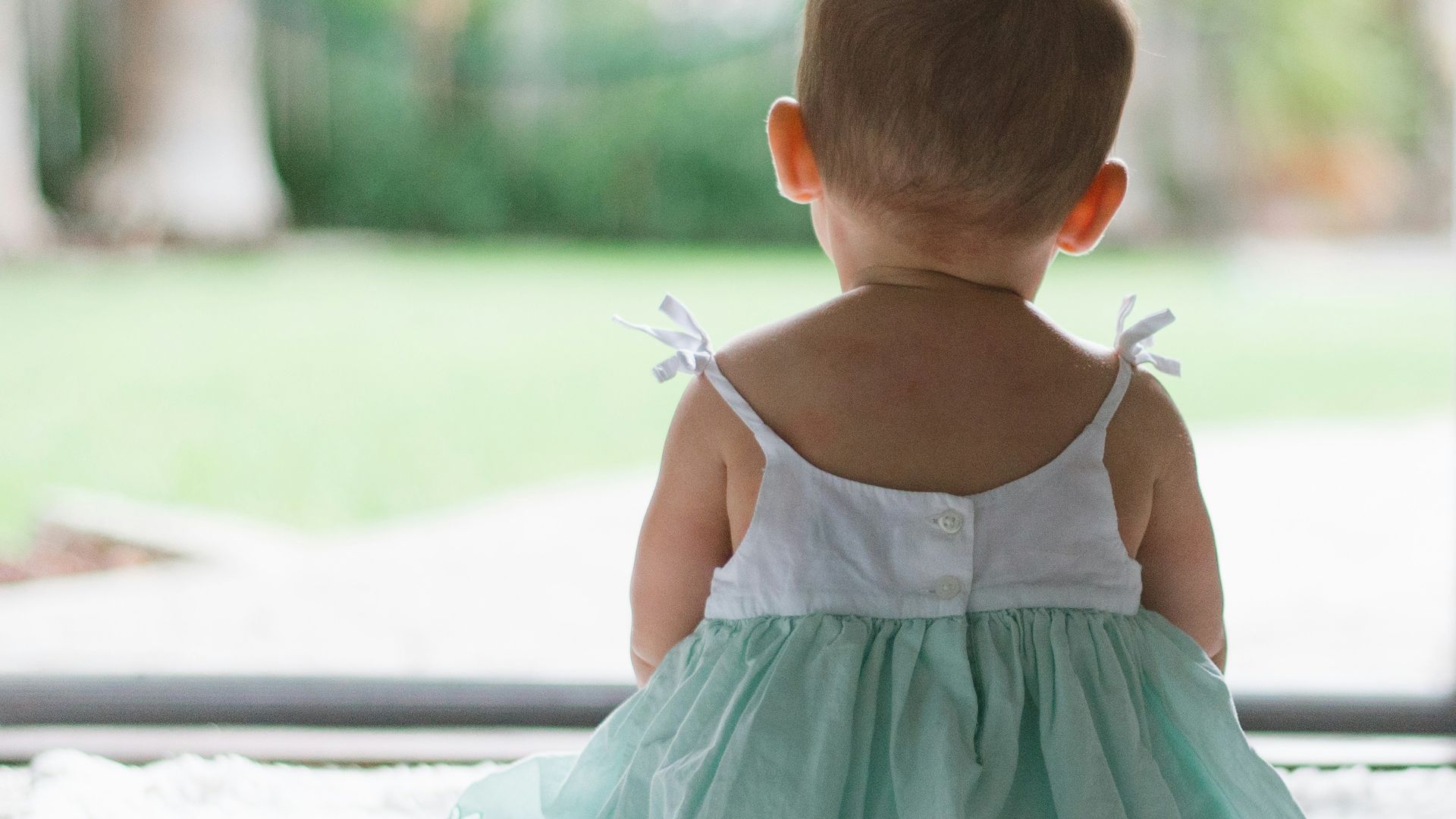 selective focus photo of toddler wearing sleeveless dress sitting on floor