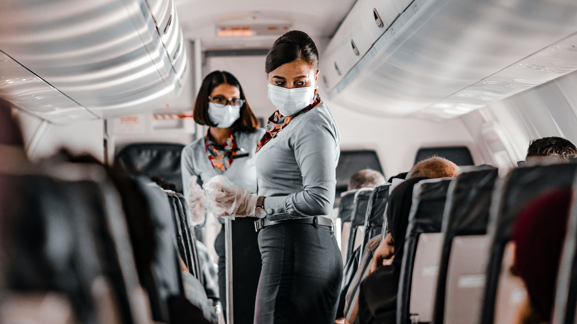 air hostess wearing a facemask standing in the aisle of an aeroplane