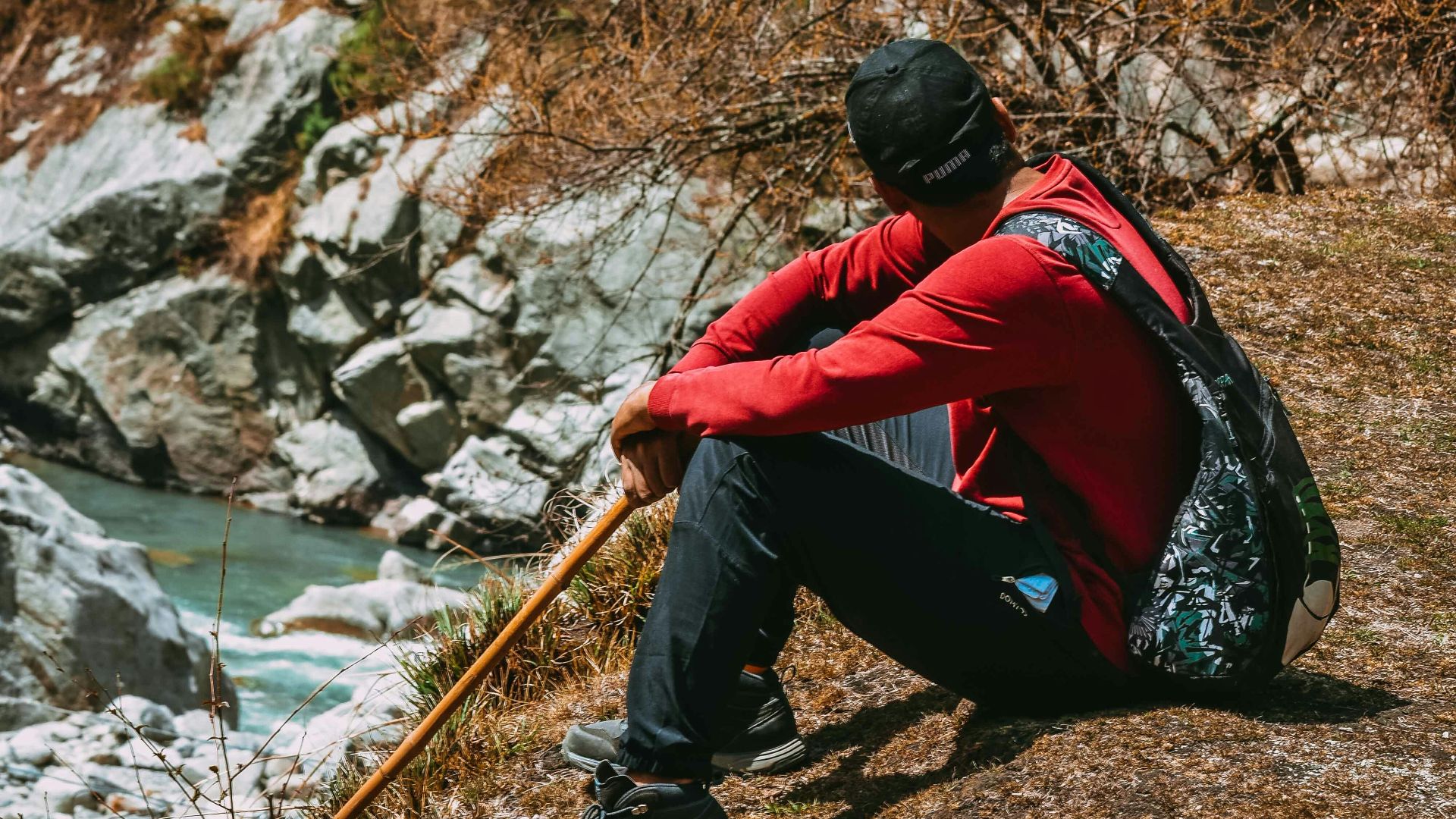 man in red and black jacket sitting on rock near river during daytime
