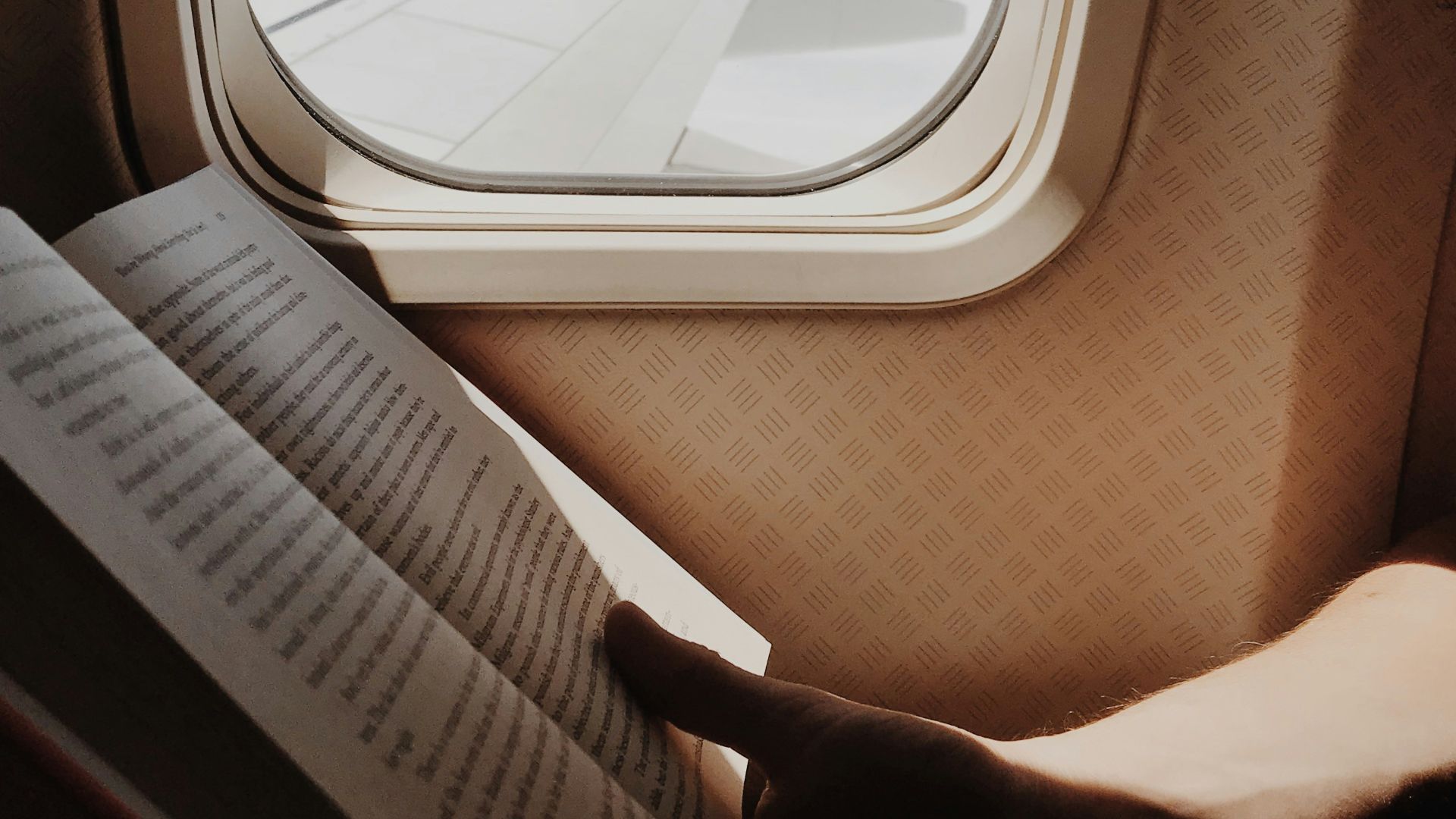person reading book beside airplane window