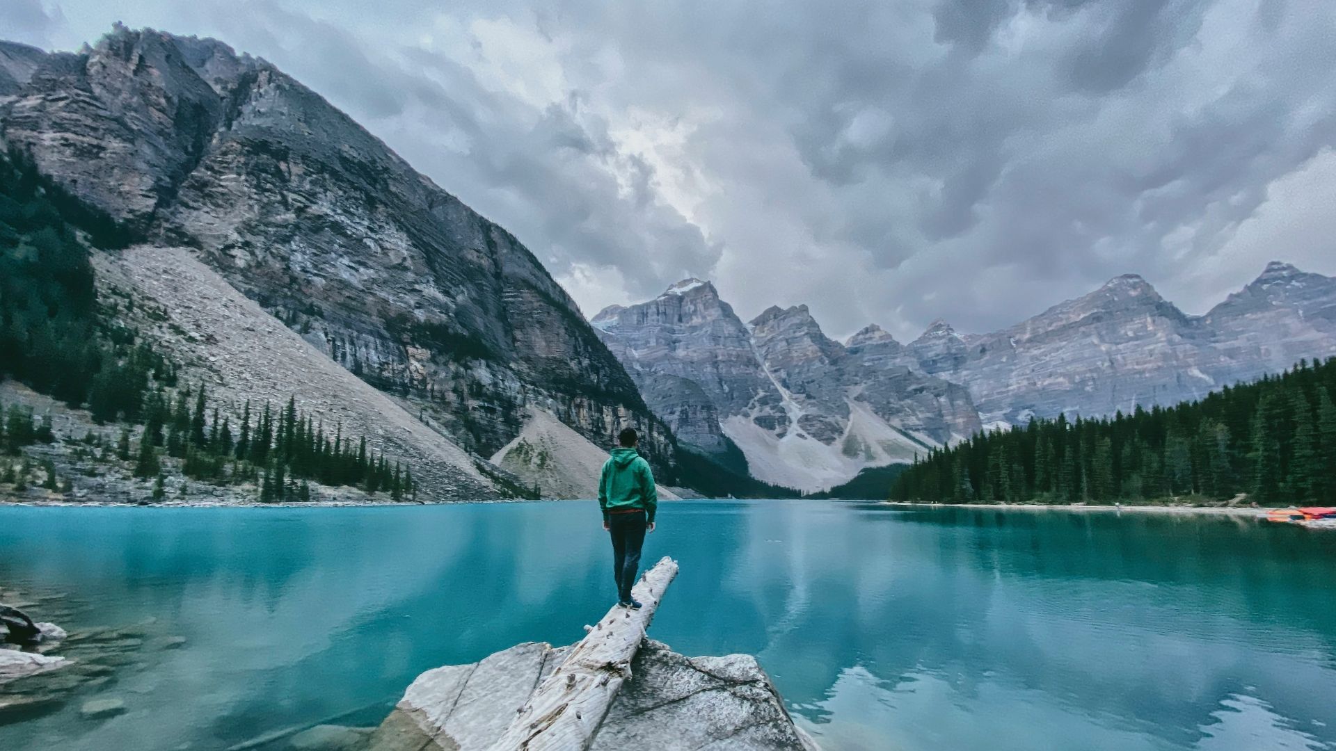 person in green jacket and black pants standing on rock near lake during daytime