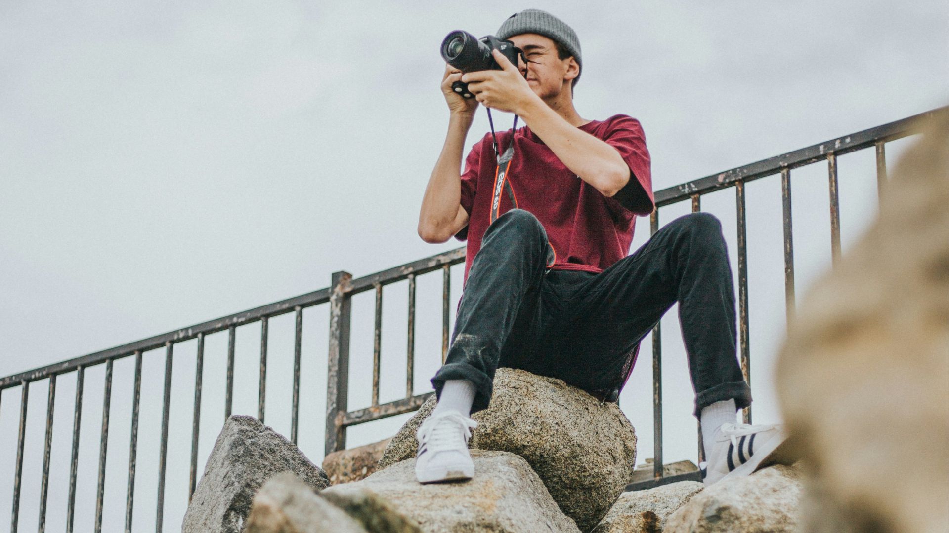 person sitting on rock holding black DSLR camera
