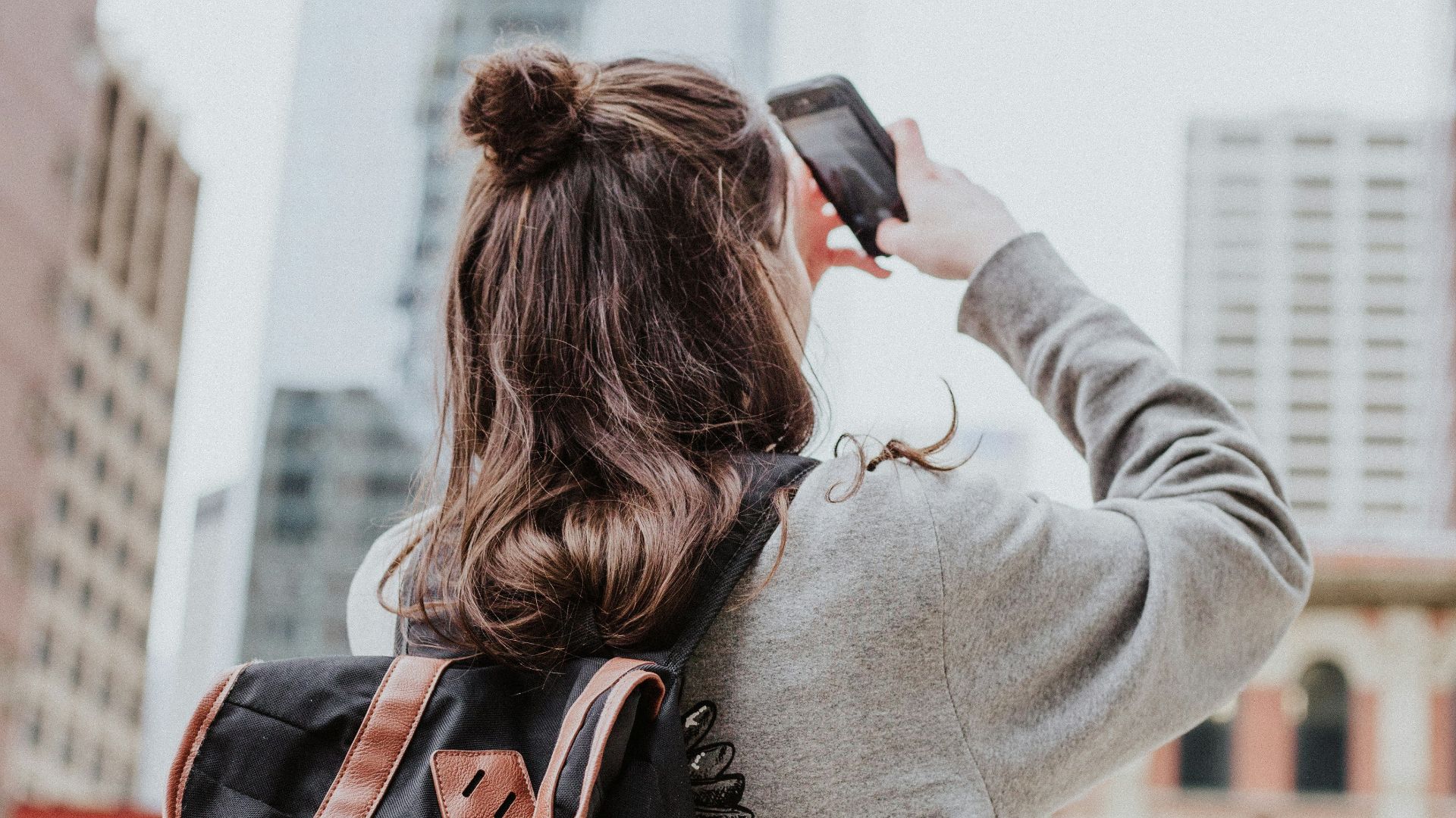 woman taking photo of high-rise building beside road