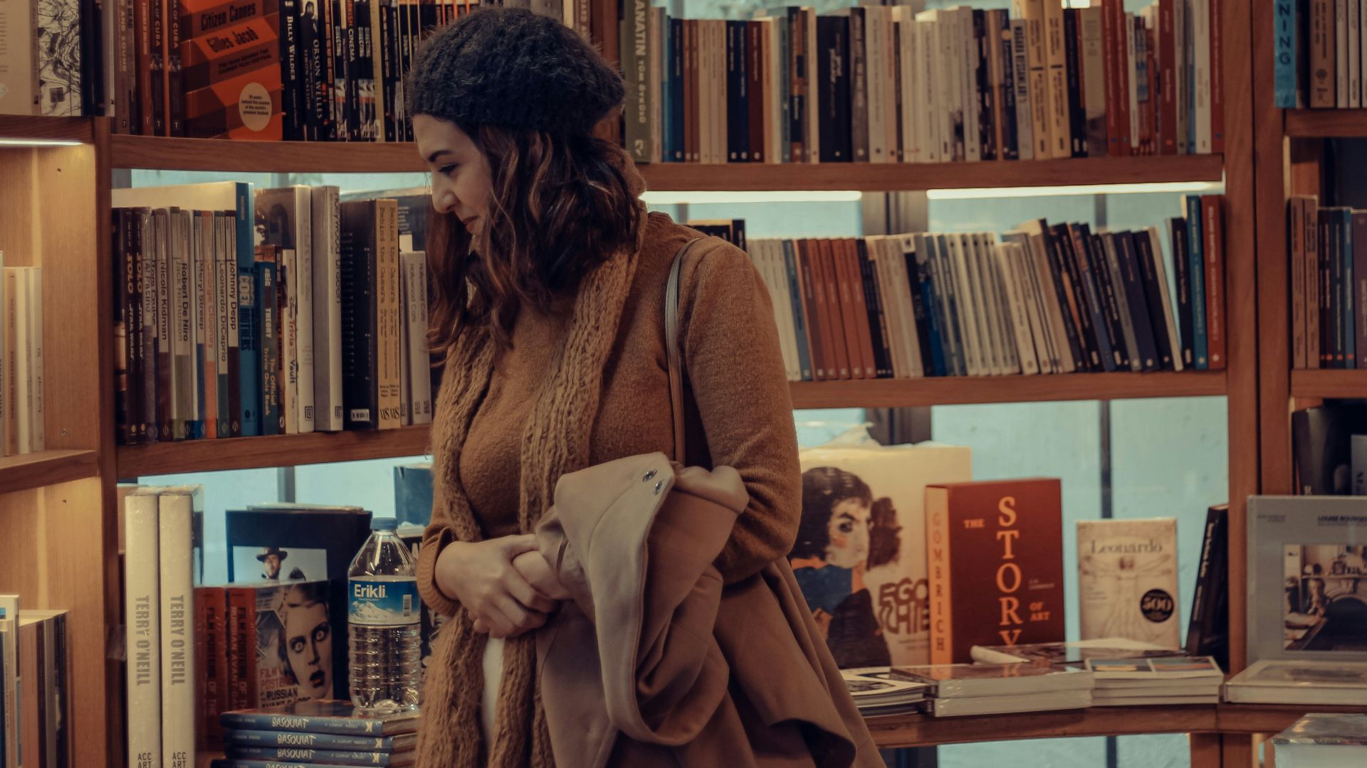 woman in brown coat reading book in library
