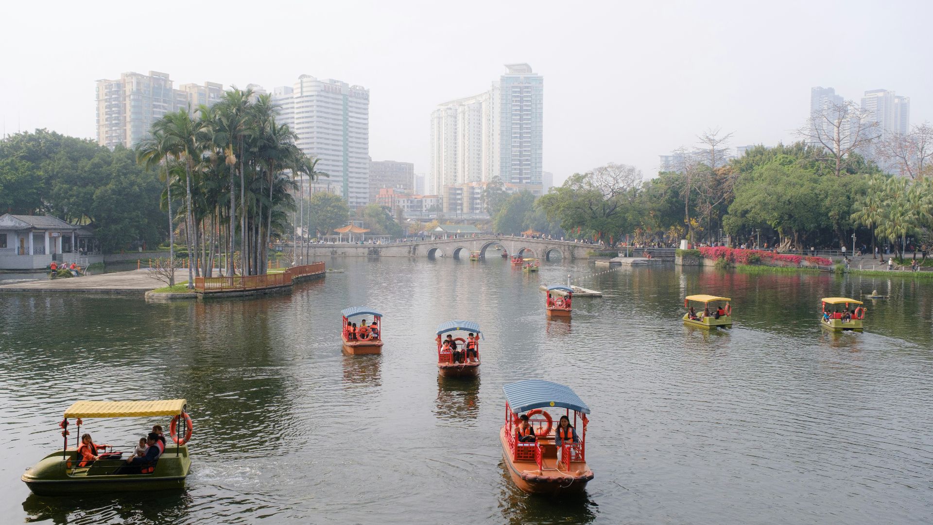 Boats sail across a lake in front of buildings.