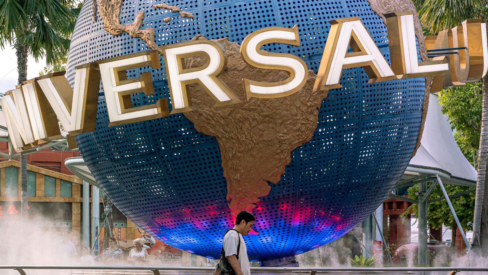 man in black jacket walking on sidewalk with blue and yellow heart shaped balloon
