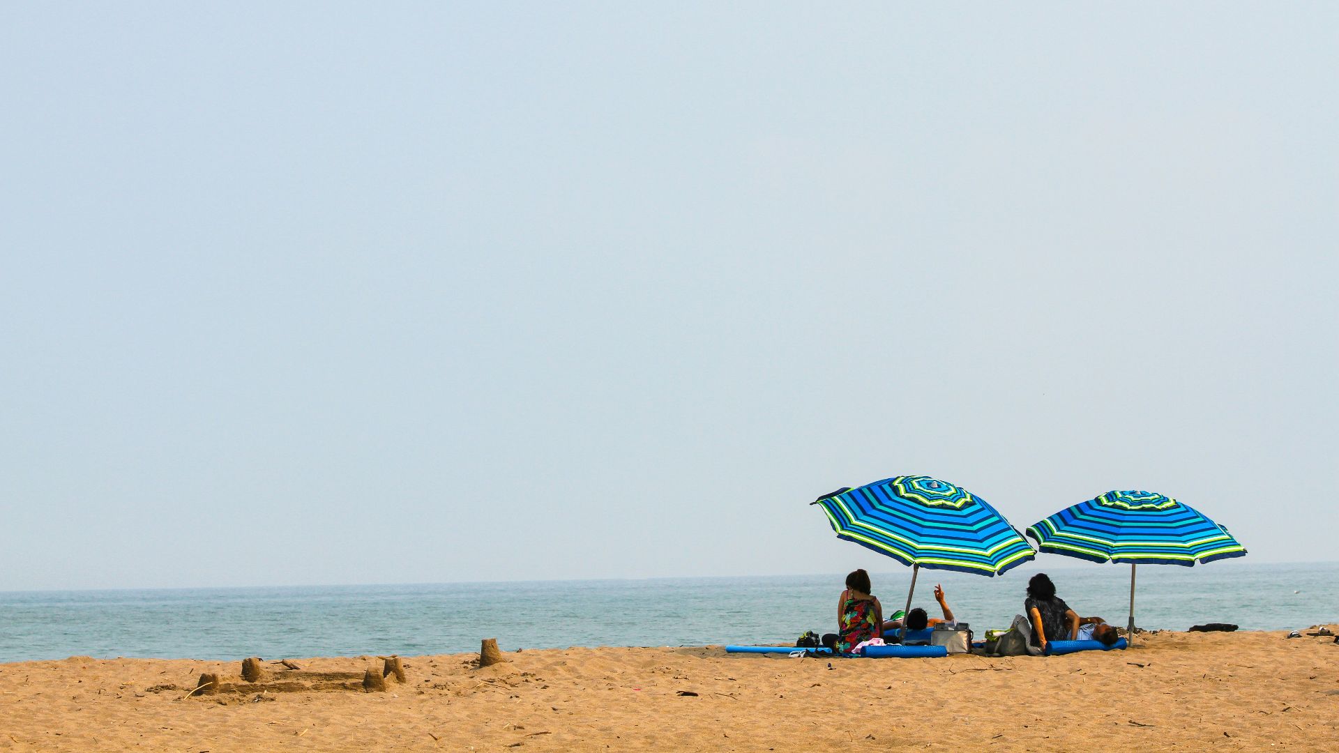 people lying on mat under green and blue umbrella during daytime