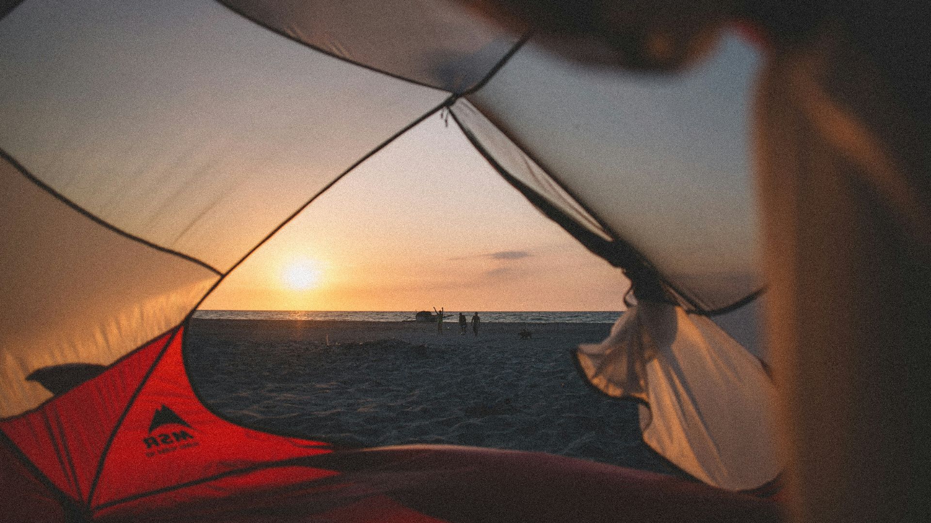 person in white shirt holding white and red umbrella near body of water during sunset