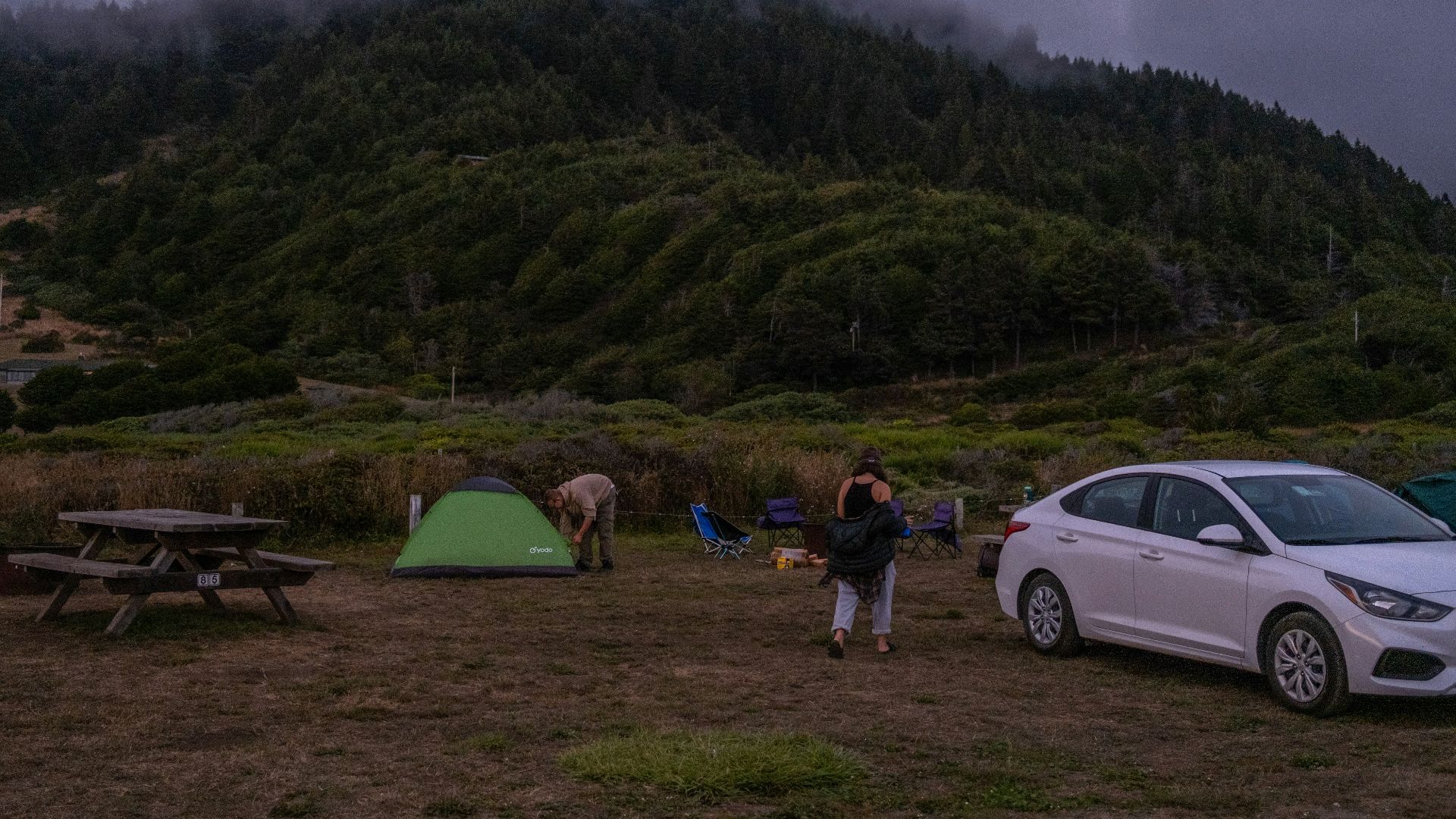 a woman and a man standing next to a tent and a car