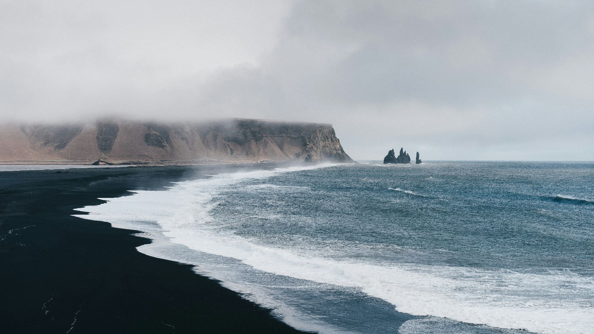 black sand near body of water under the cloudy sky during daytime