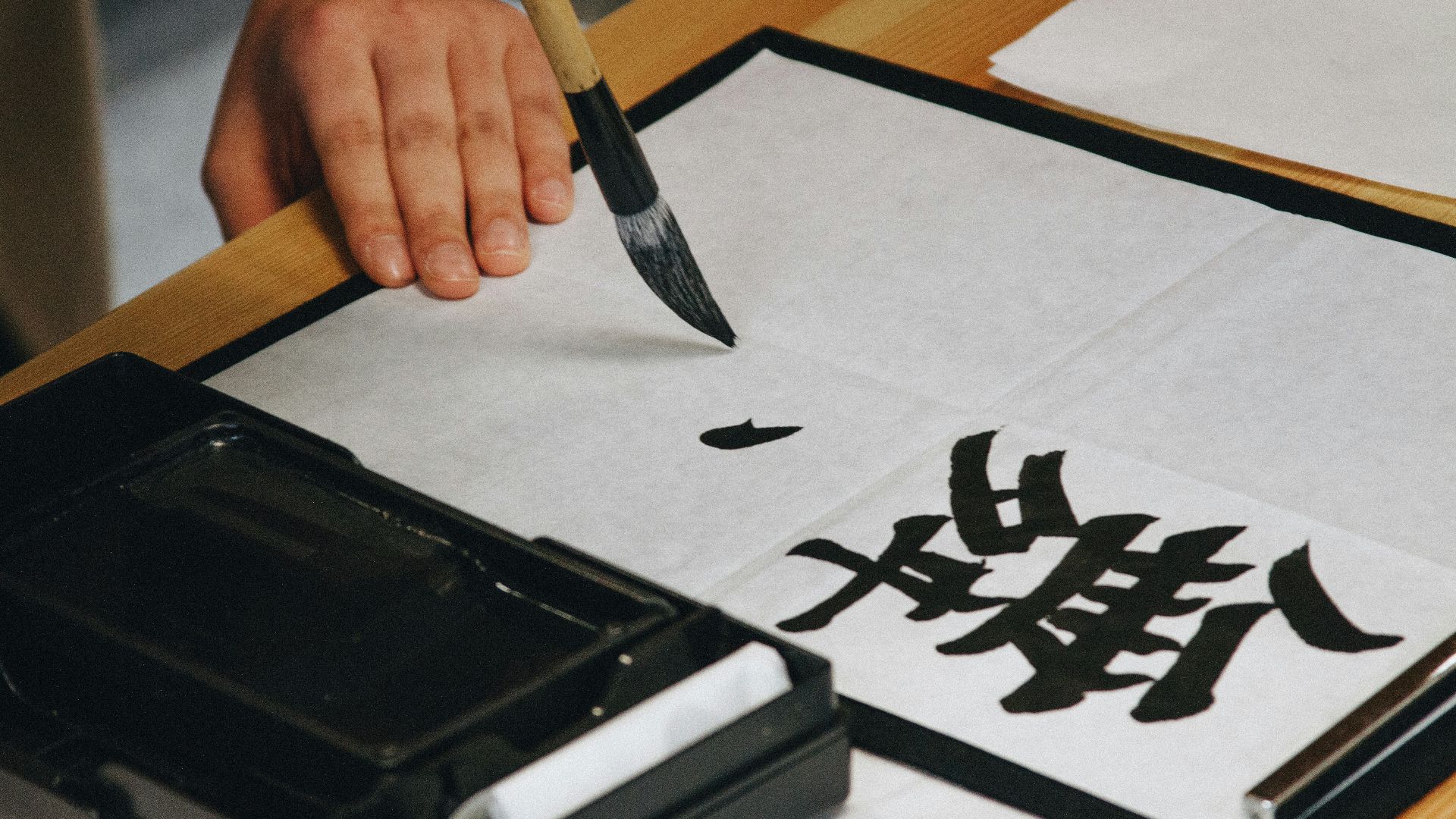 person holding black paint brush while painting black text on white paper