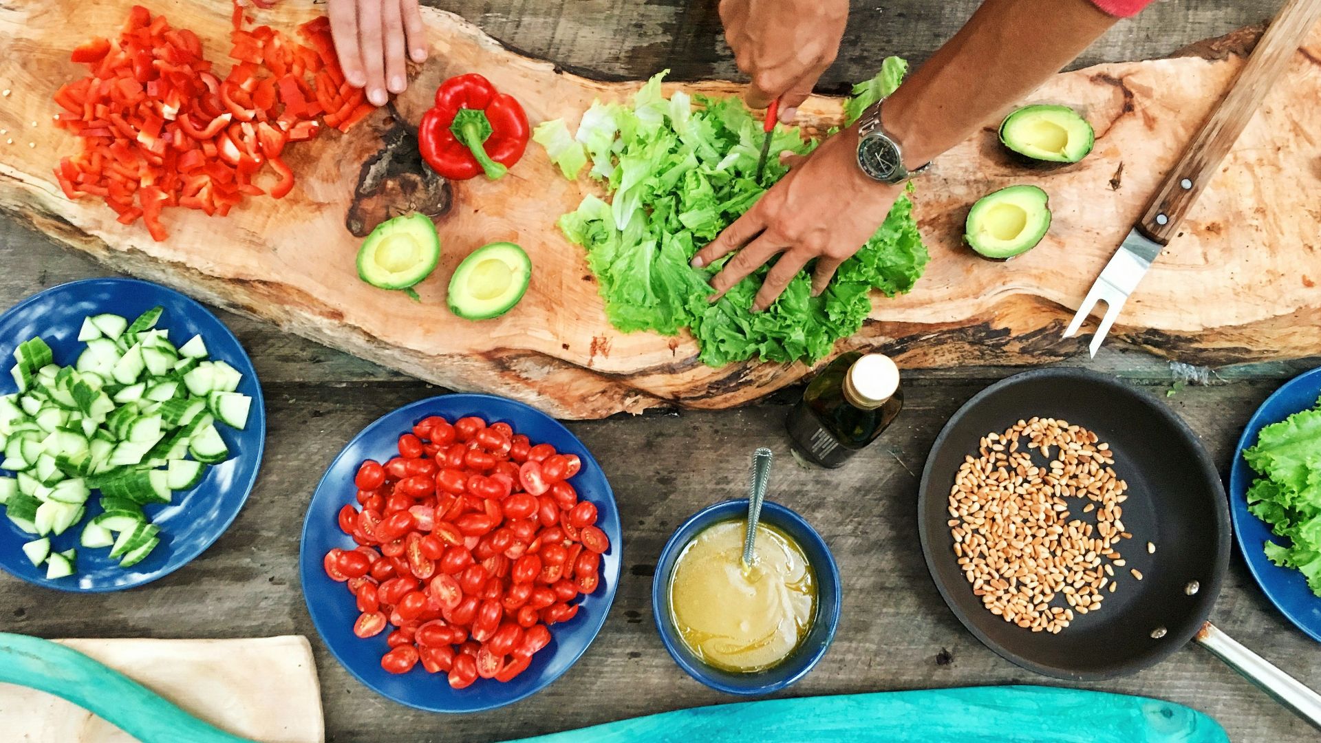person slicing green vegetable in front of round ceramic plates with assorted sliced vegetables during daytime