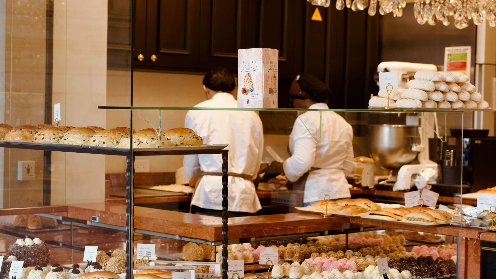 Pastry display case with chefs preparing food in background.