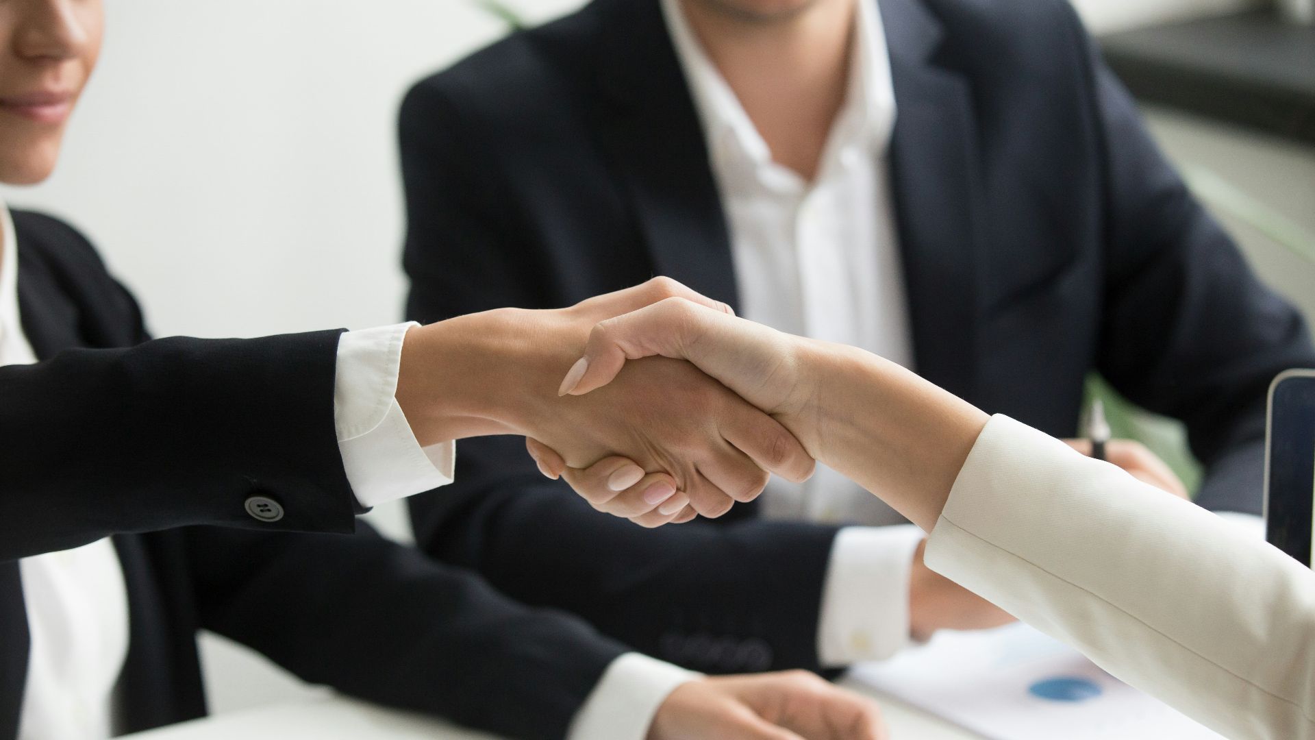 two people shaking hands in front of a laptop