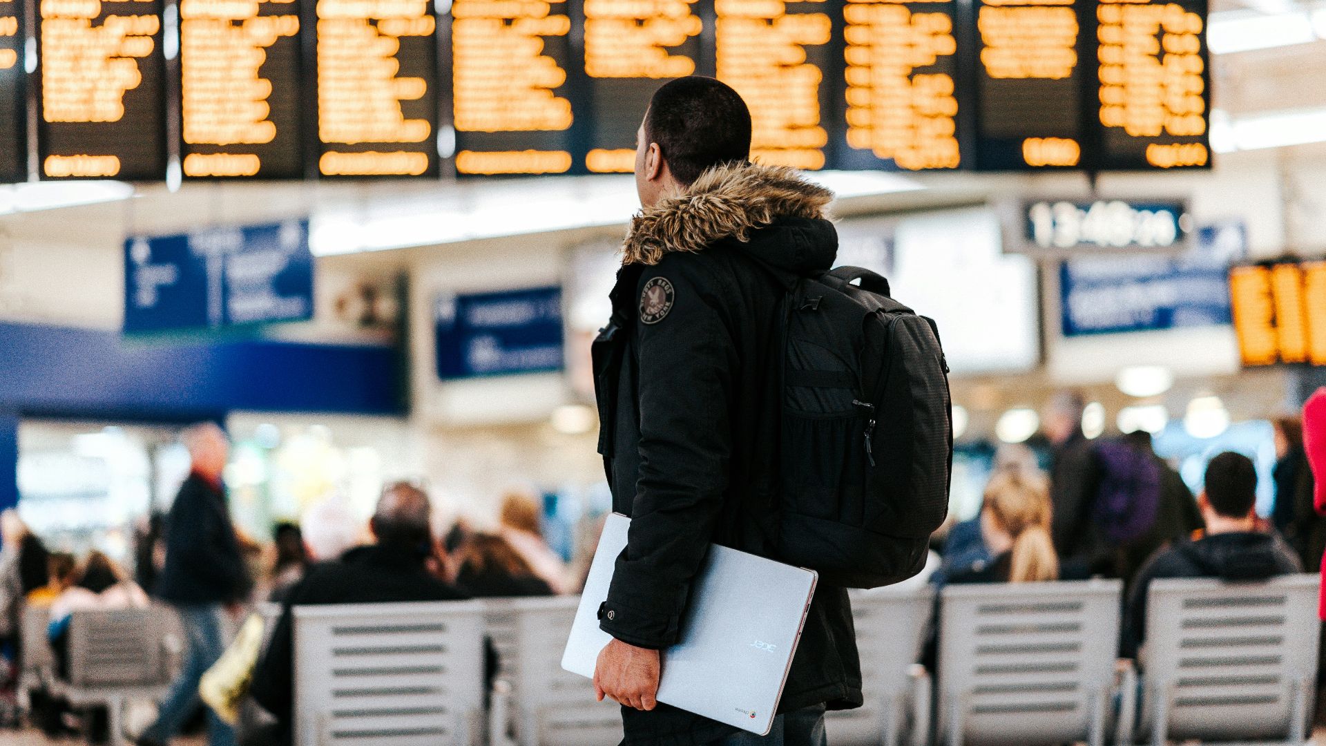 man standing inside airport looking at LED flight schedule bulletin board