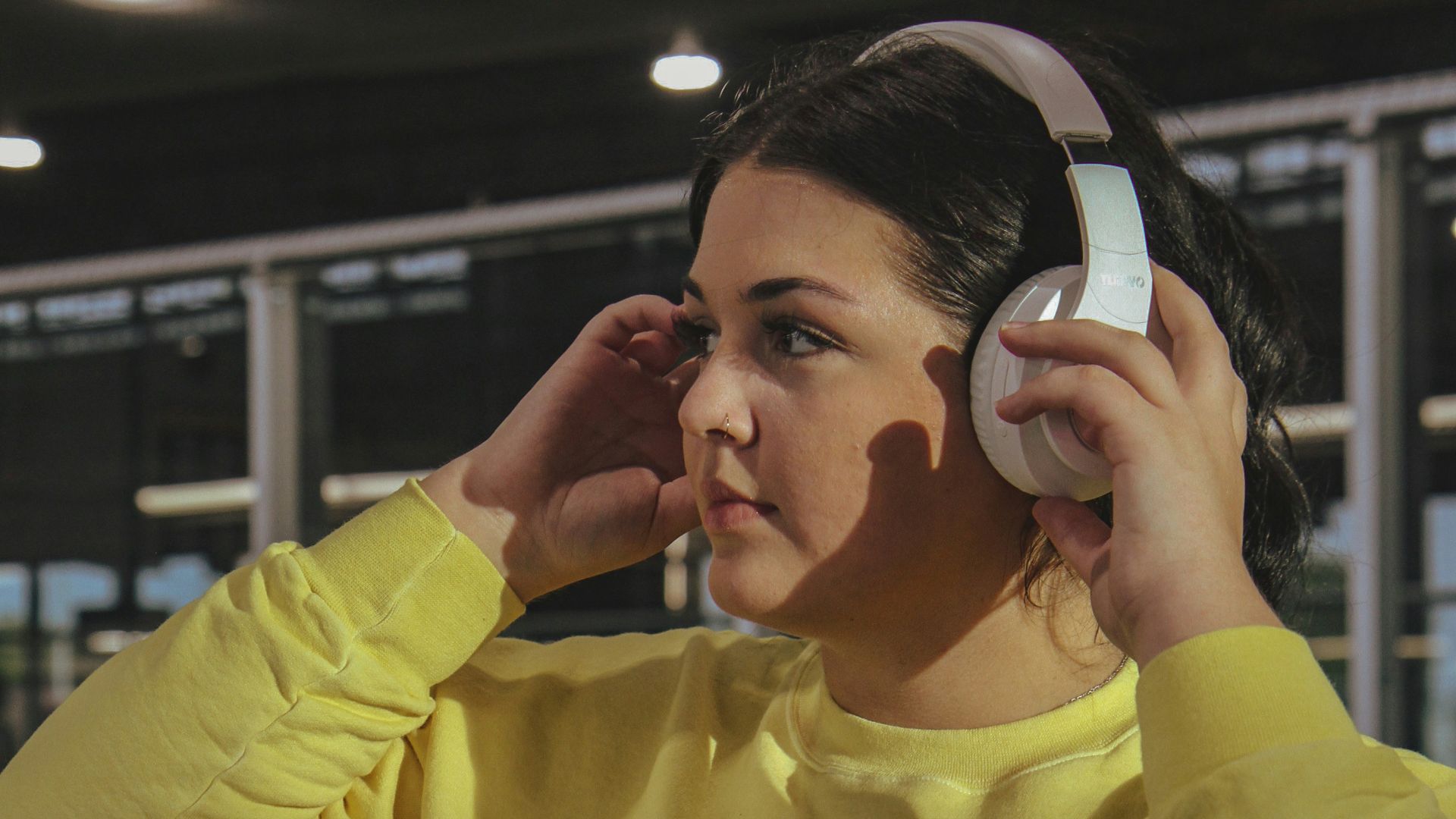 a woman in a yellow sweatshirt listening to headphones