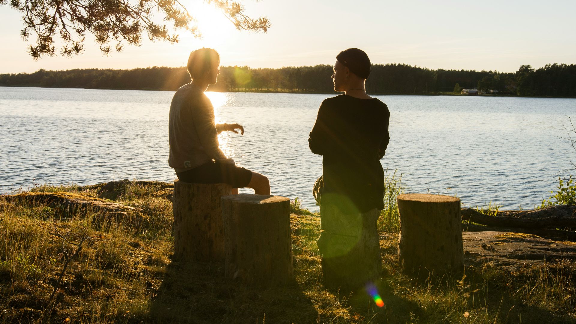 man in black jacket standing beside body of water during sunset
