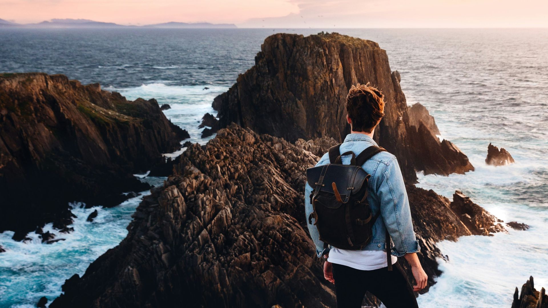 man standing near cliff looking at body of water during daytime
