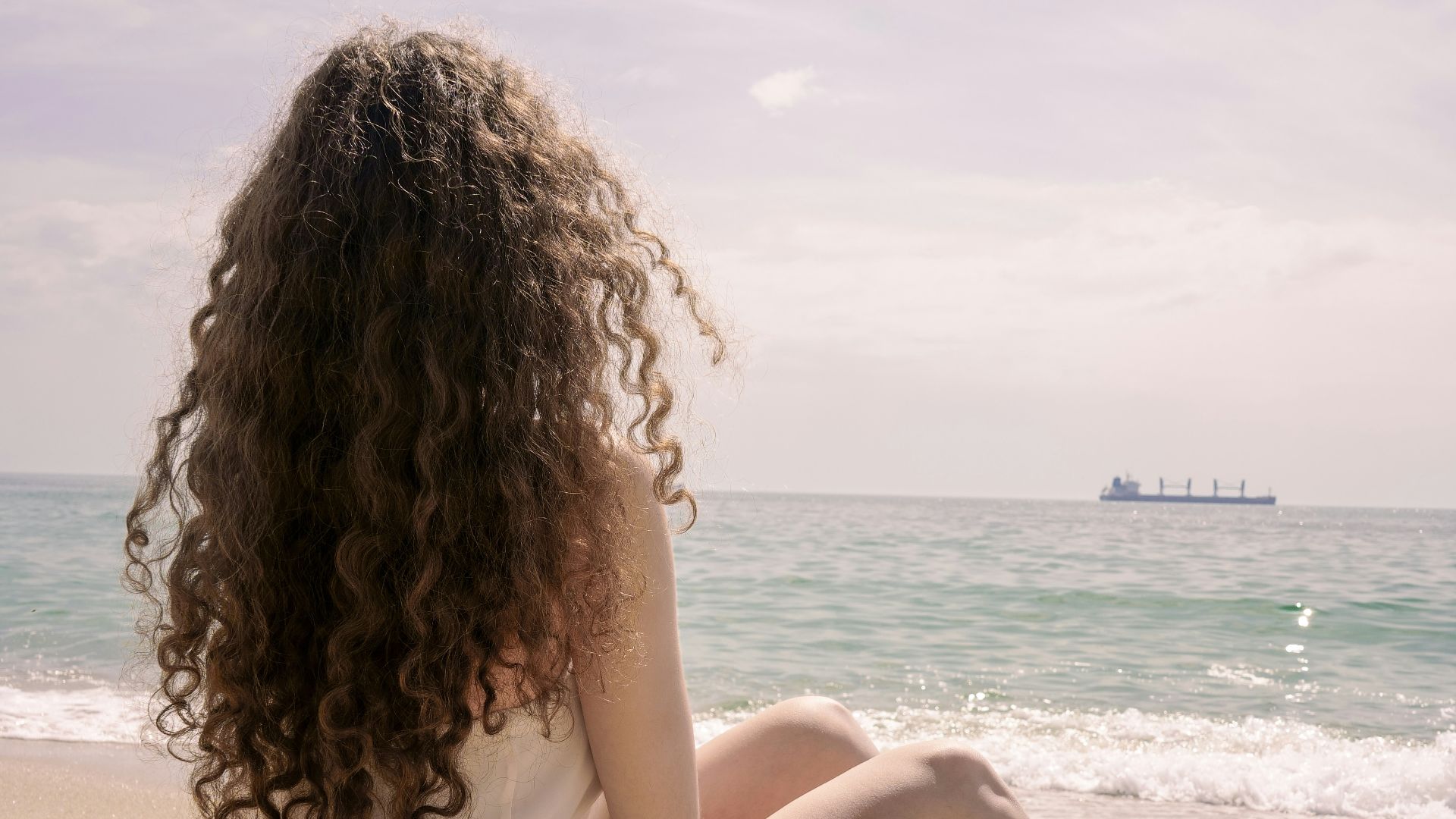 woman in white dress sitting on beach during daytime