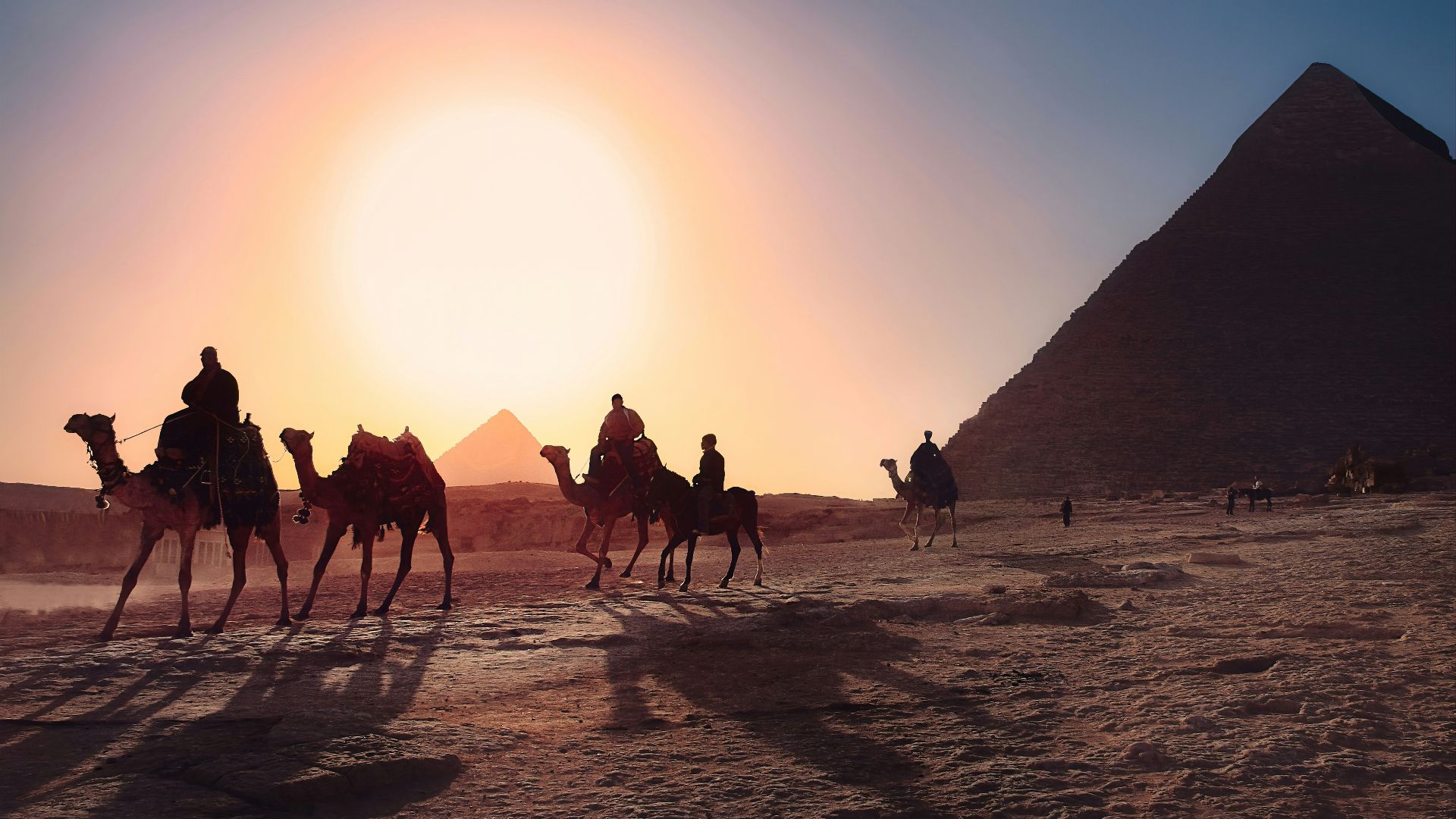 five persons riding camels walking on sand beside Pyramid of Egypt