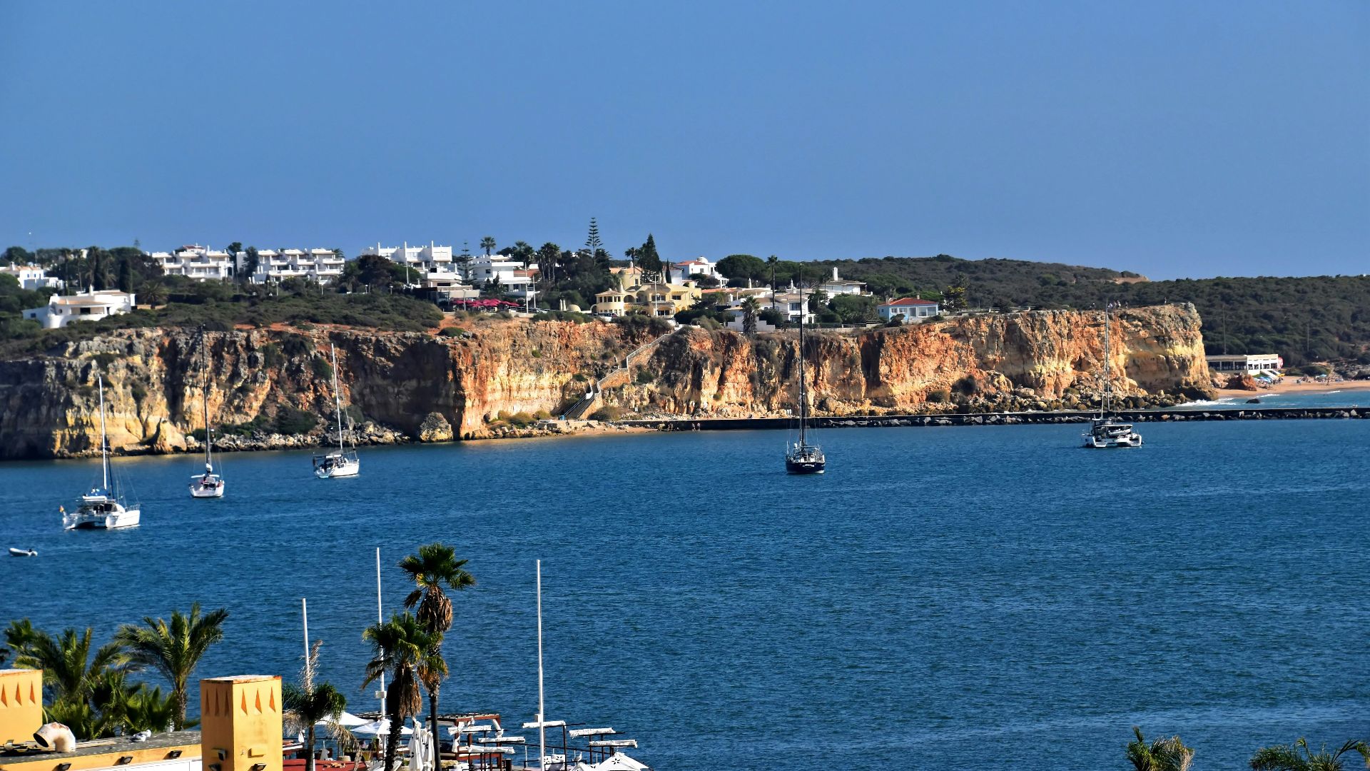 Boats sail on blue water near rocky cliffs and town.