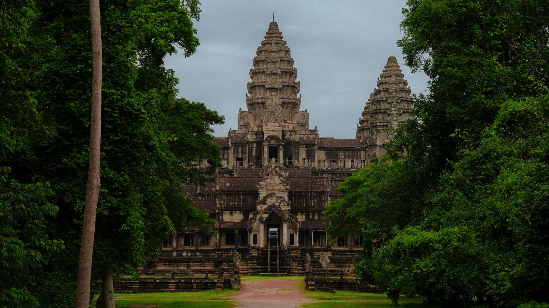 Angkor wat temple is framed by lush green trees.