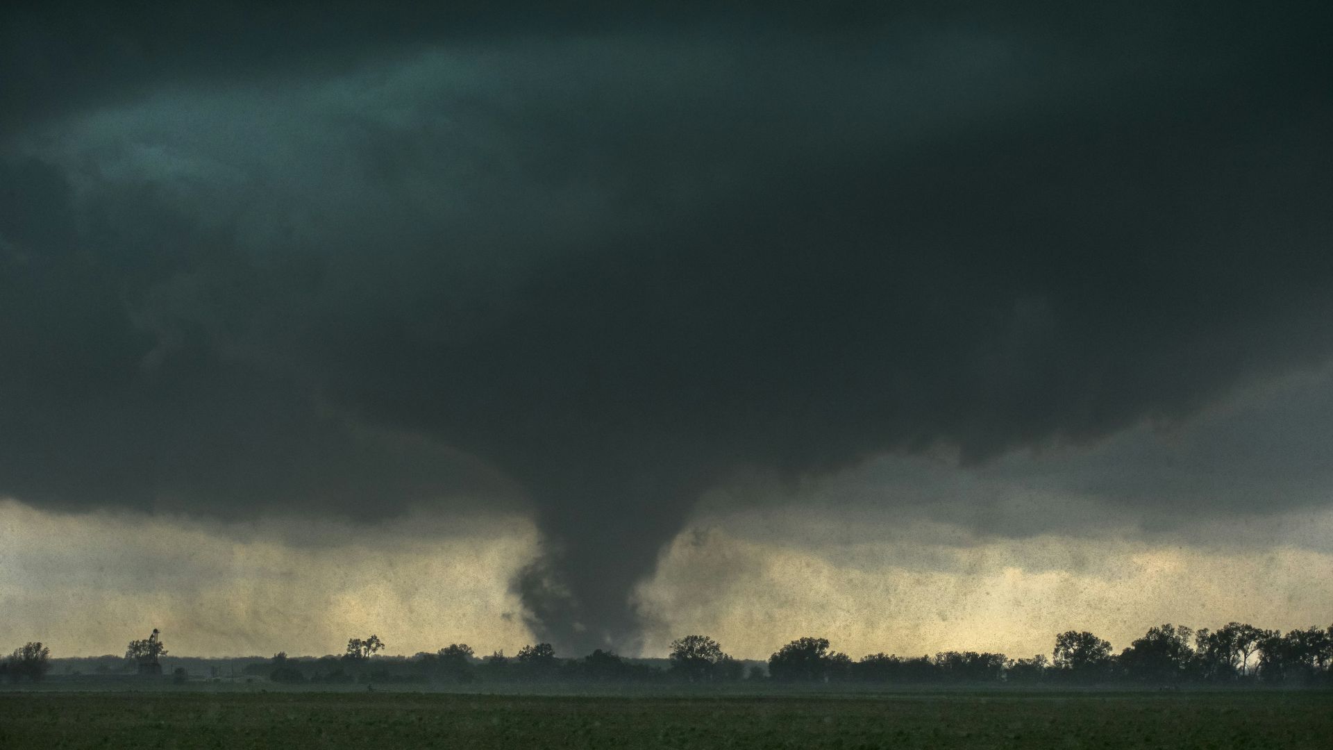 a large black cloud is in the sky over a field